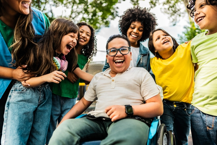 Grupo de crianças diversas e felizes brincando ao ar livre com um menino cadeirante