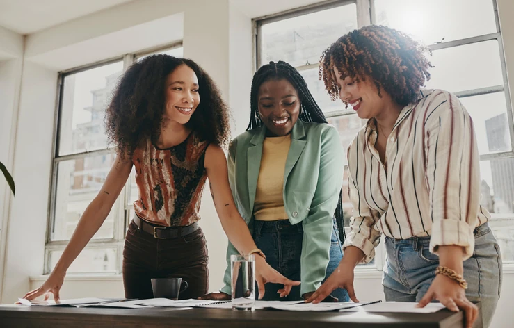 Três mulheres jovens e diversas colaborando em um projeto em um escritório iluminado