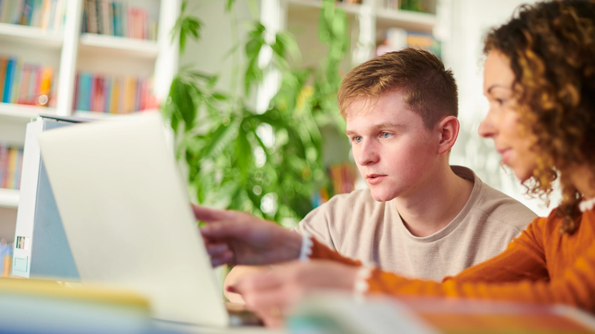 Estudantes jovens utilizando laptop para pesquisas acadêmicas e estudos colaborativos em um ambiente de biblioteca iluminado