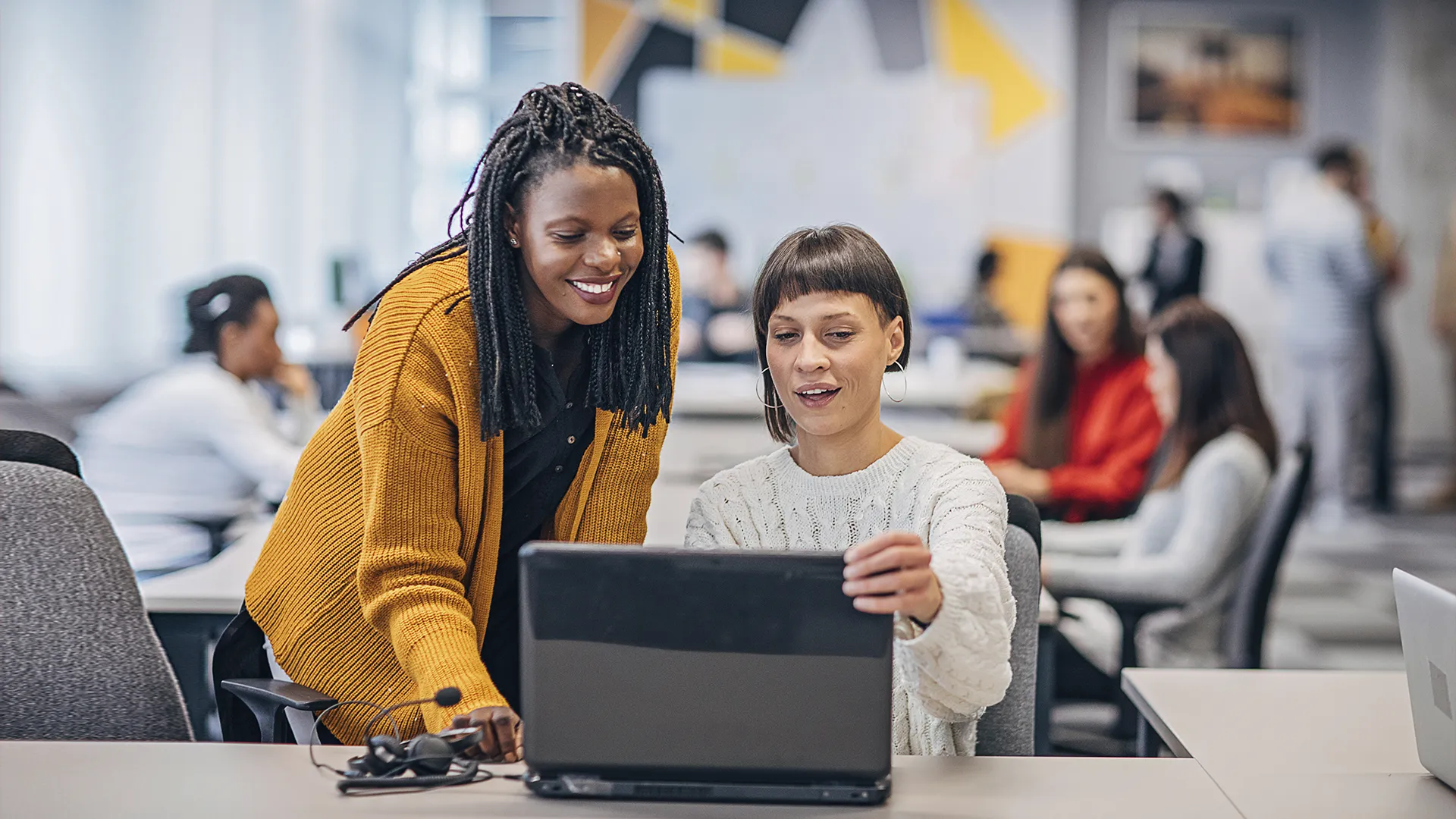 Duas colegas de trabalho colaborando em um notebook em um escritório moderno