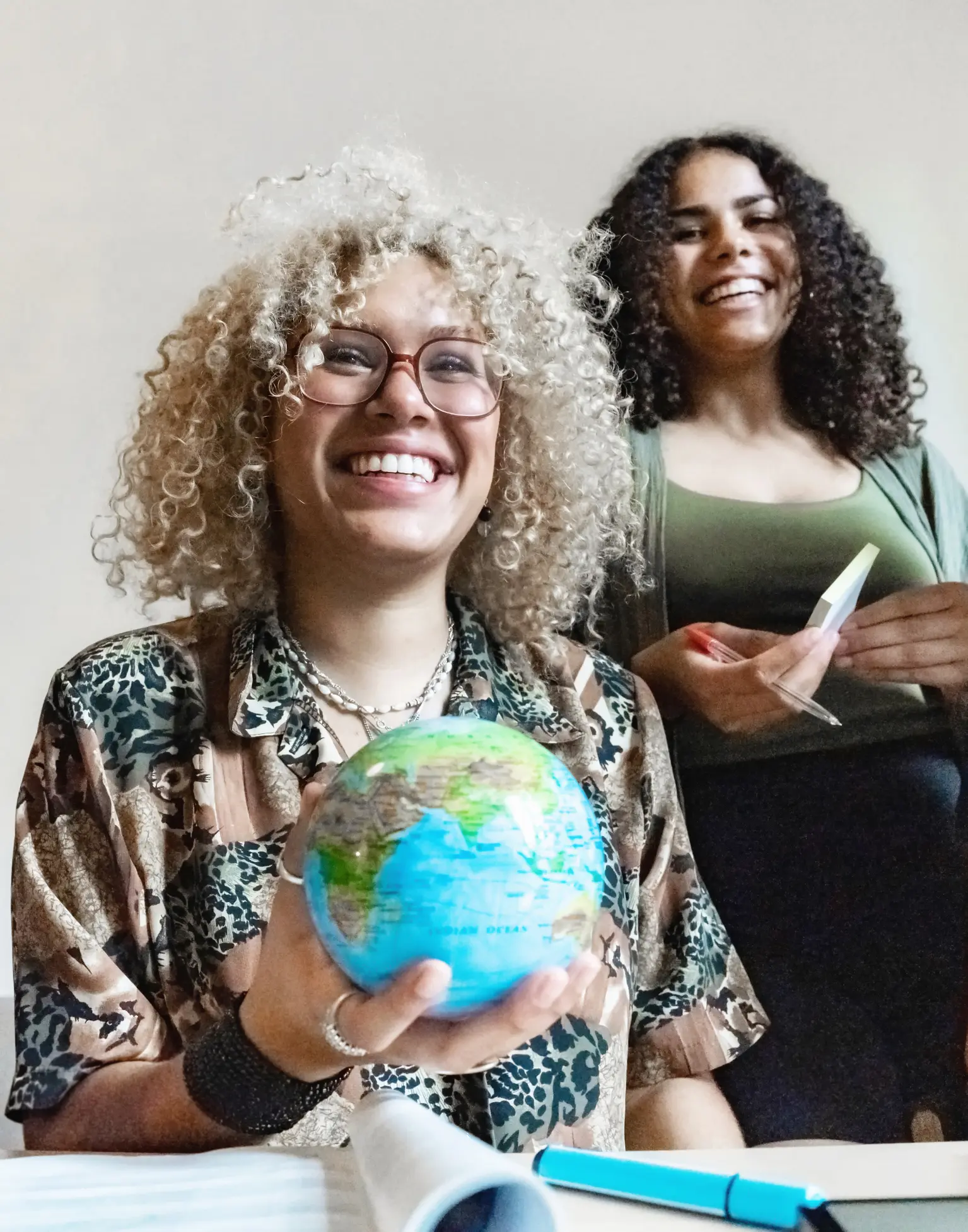 Duas estudantes universitárias sorridentes segurando um globo terrestre em uma mesa de estudos