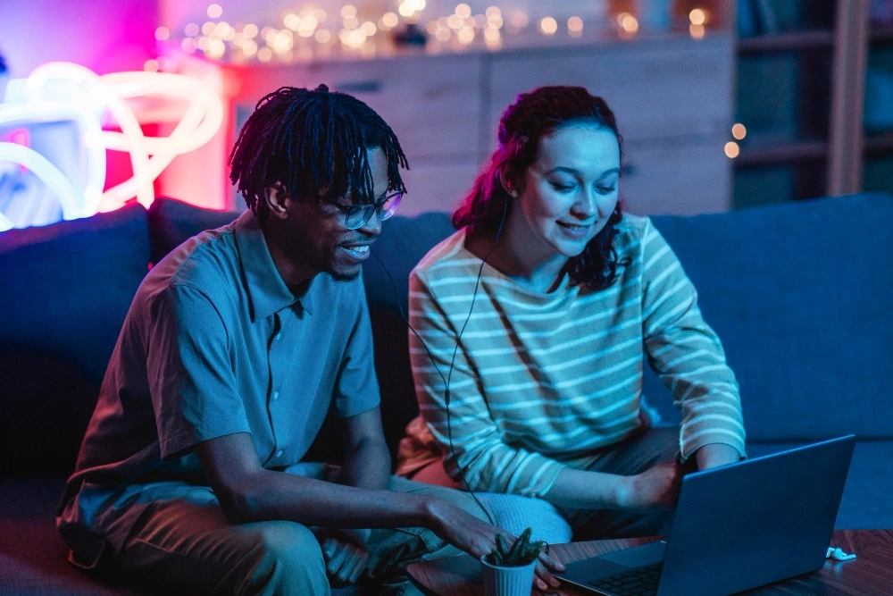 Jovem casal estudante utilizando notebook para estudo online em ambiente com iluminação neon
