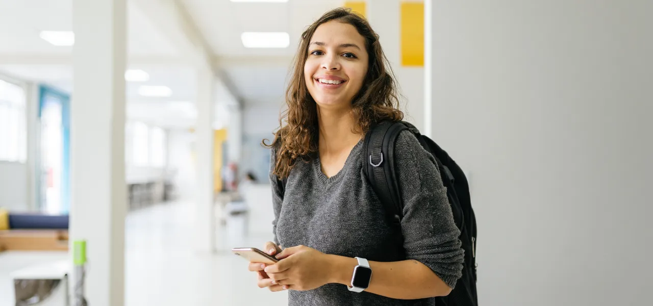 Estudante universitária sorridente segurando um smartphone no campus