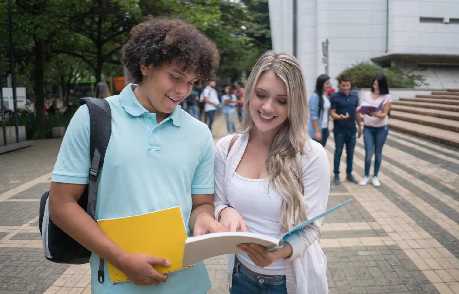 Estudantes universitários sorridentes conversando e revisando cadernos em um campus acadêmico
