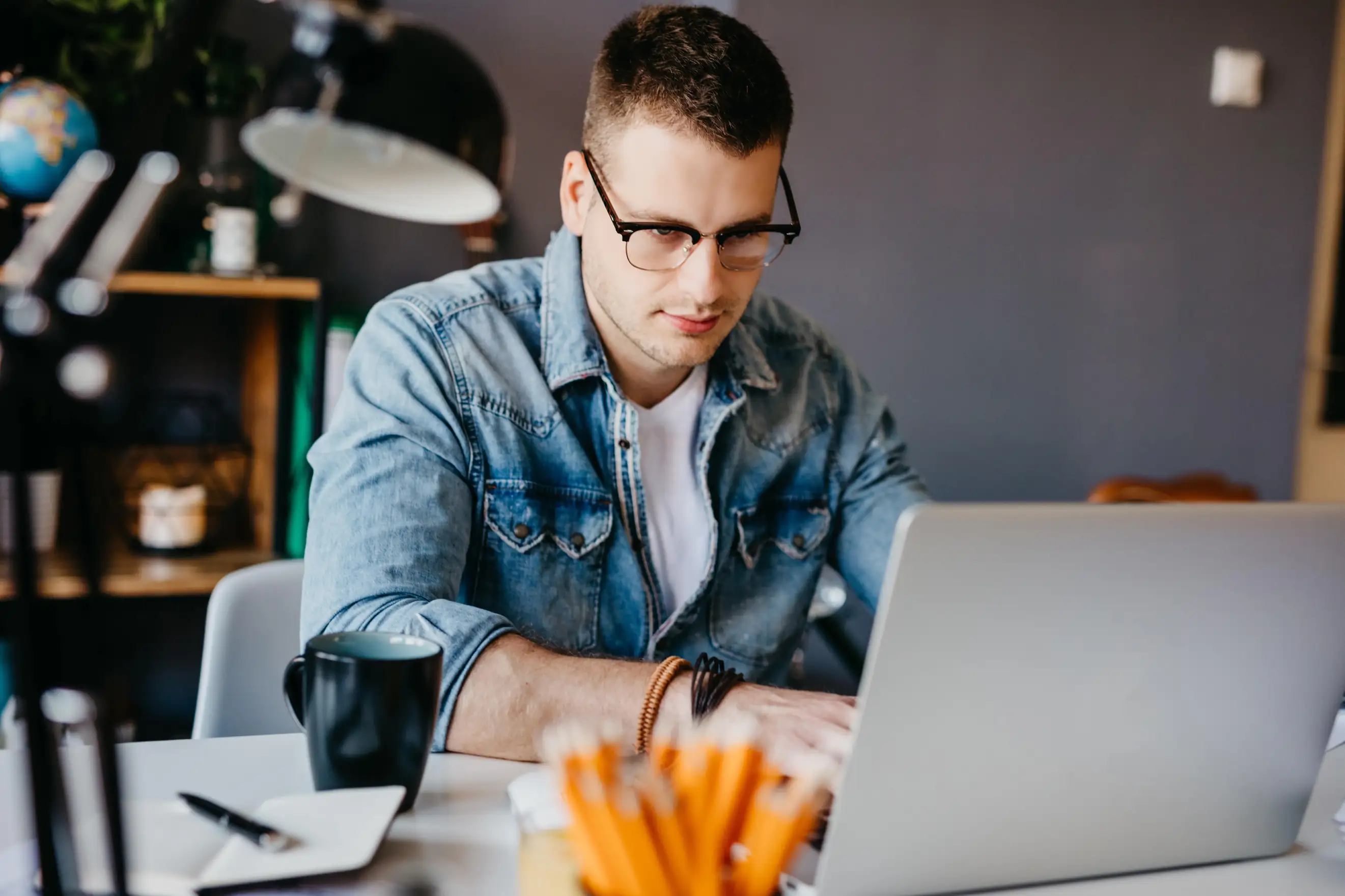 Profissional focado utilizando notebook para realizar tarefas de trabalho e estudos em um ambiente de escritório produtivo Homem jovem de óculos trabalhando em um notebook em um escritório moderno
