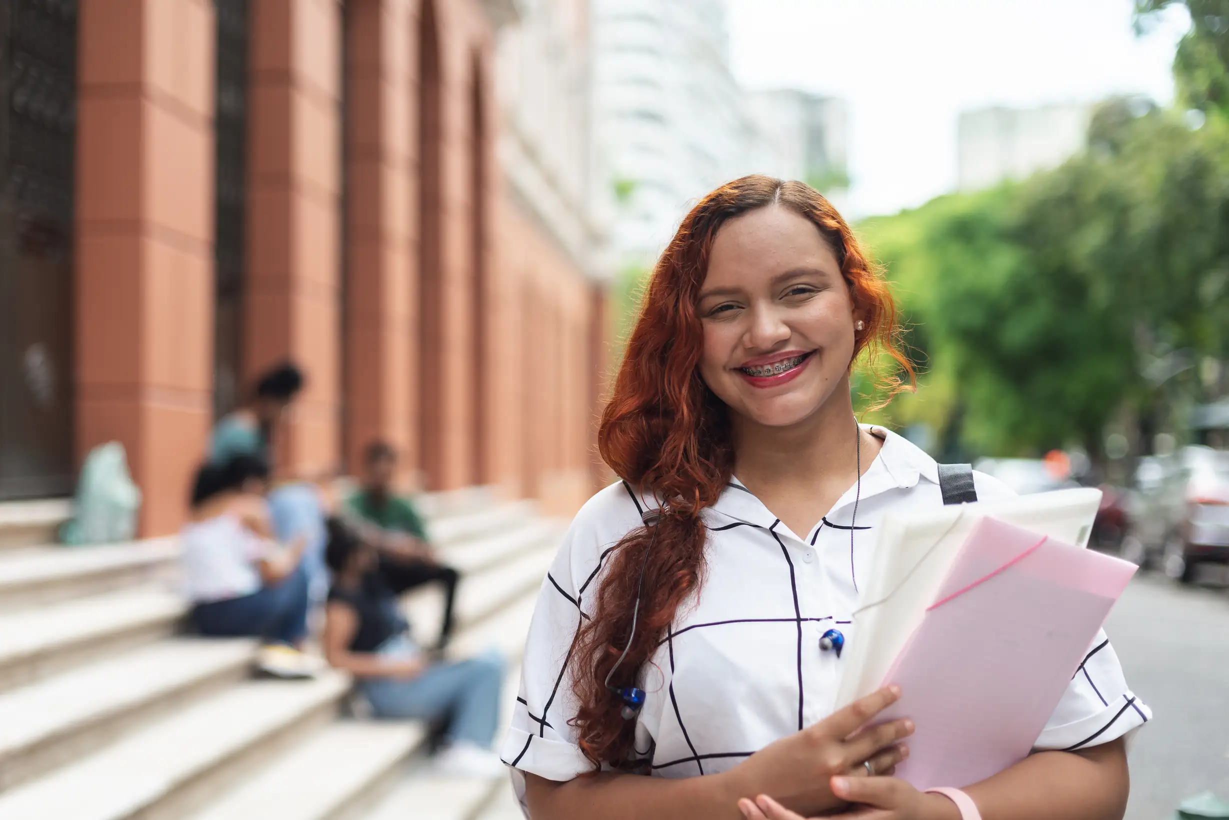 Estudante universitária sorridente segurando cadernos e materiais escolares em um campus