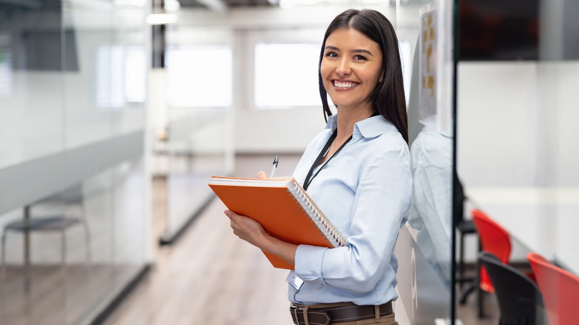 Jovem profissional focada e sorridente segurando um caderno em ambiente corporativo ou educacional moderno para ilustrar sucesso e aprendizado
