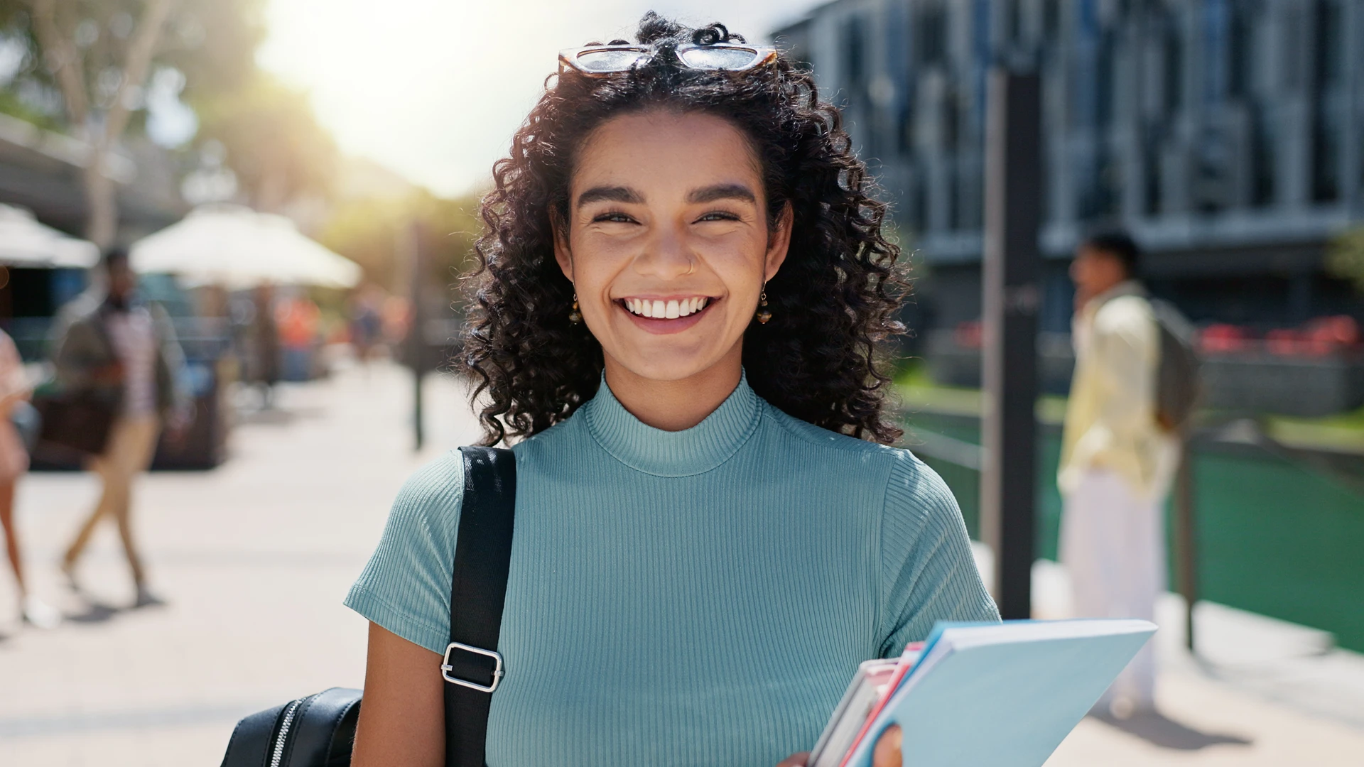 Estudante universitária sorridente carregando cadernos em um campus ao ar livre