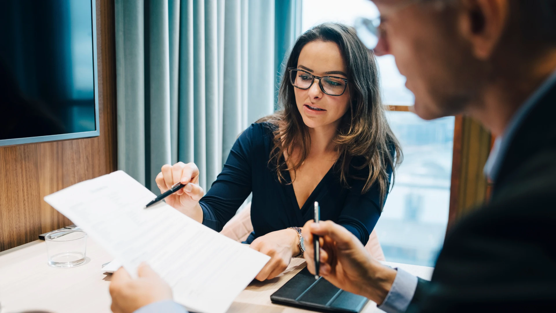Mulher de negócios de óculos explicando um documento para um colega em uma reunião corporativa