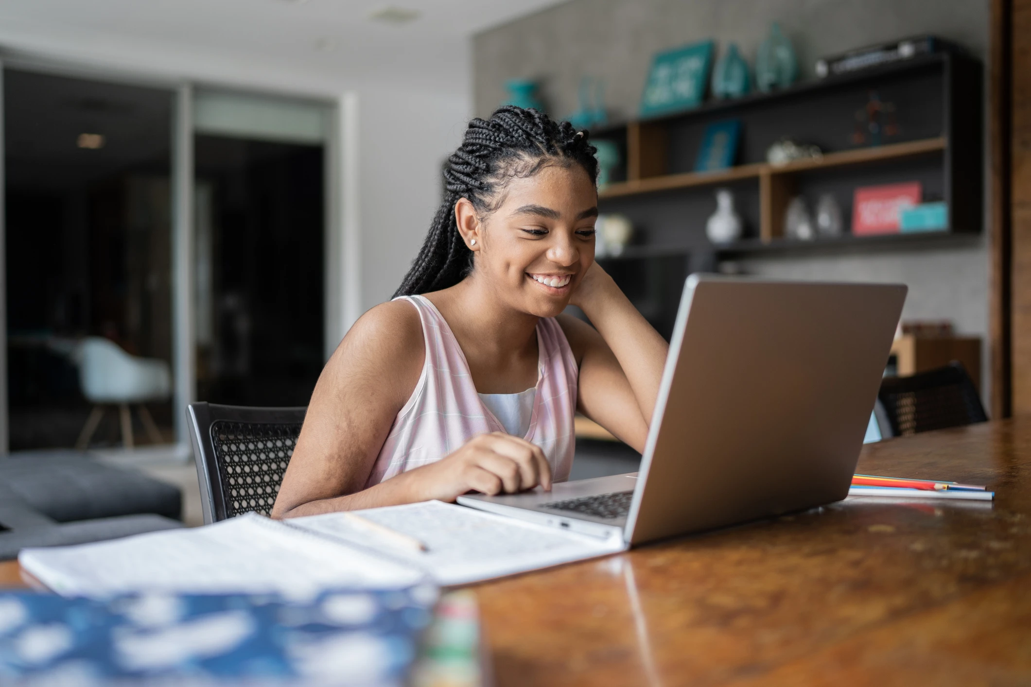 Estudante jovem sorrindo enquanto usa um notebook para estudar em casa