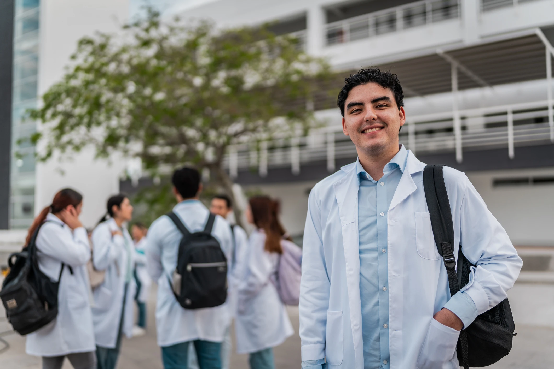 Estudante de medicina sorridente vestindo jaleco branco em frente ao campus universitário