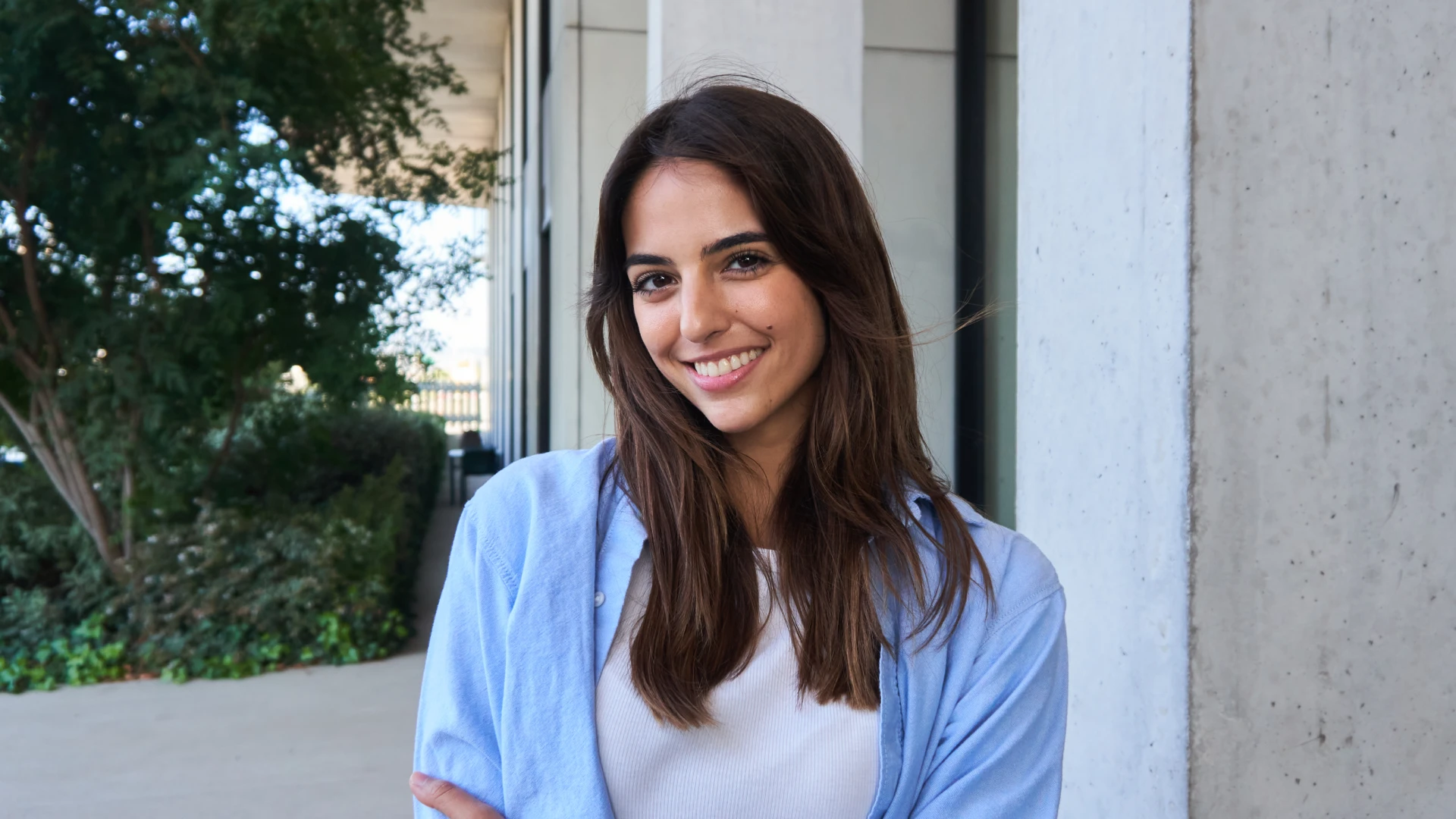 Jovem mulher sorridente com cabelos castanhos vestindo camisa azul em ambiente externo