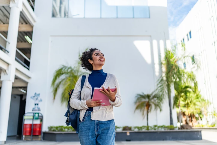 Estudante universitária sorrindo com caderno e mochila no campus