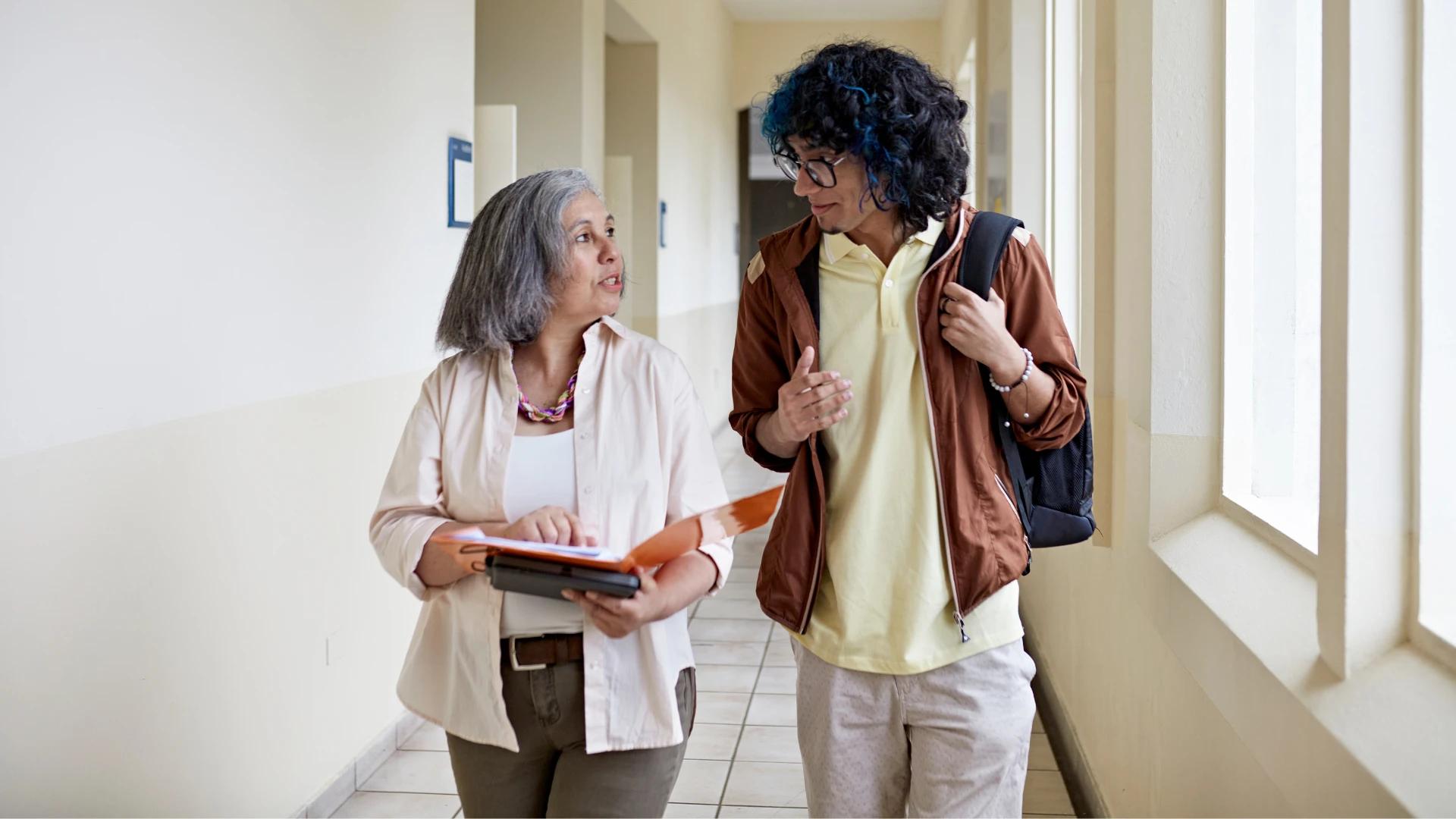 Aluno e professora andando no corredor da faculdade