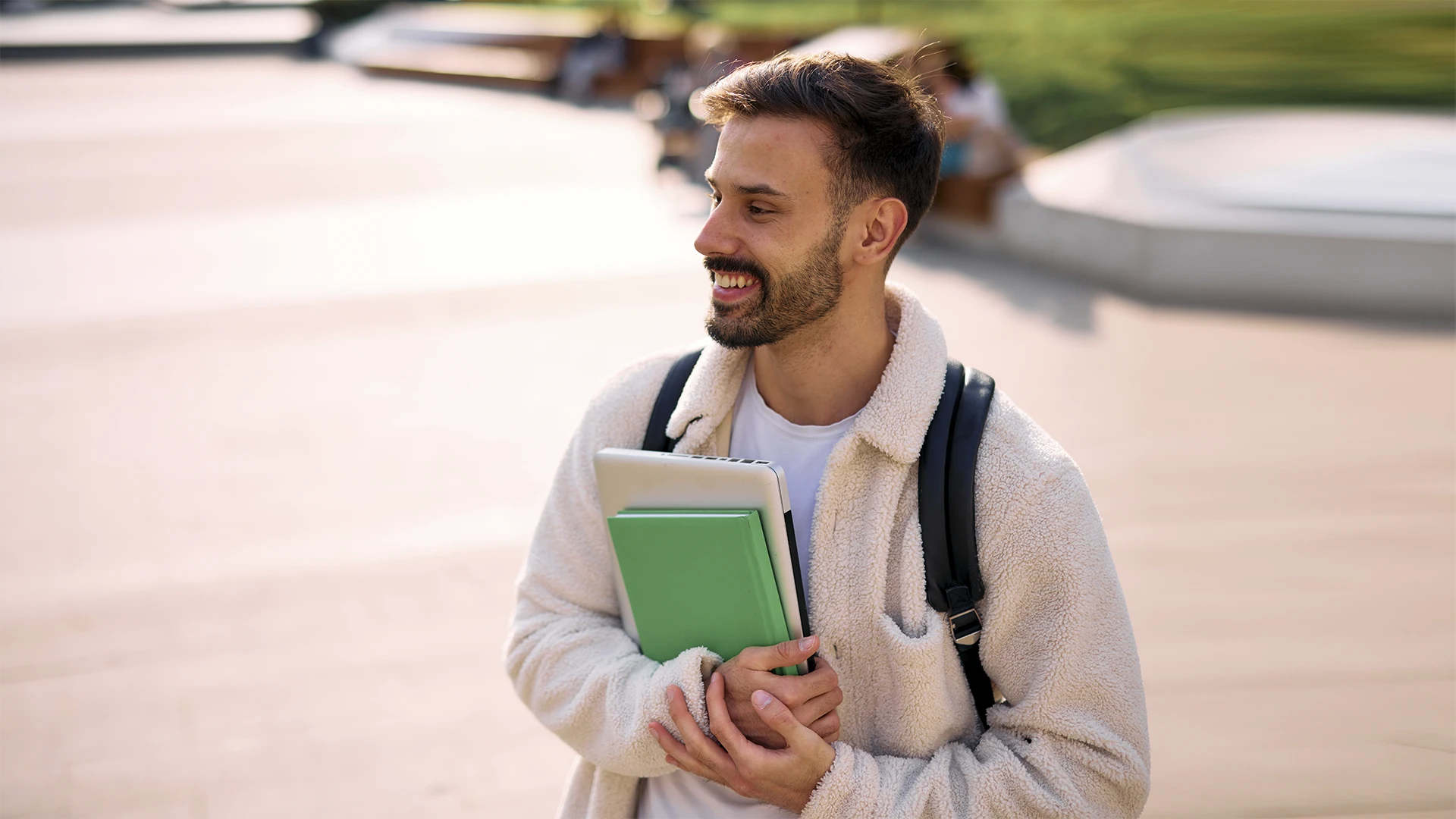 Jovem estudante universitário sorridente carregando laptop e caderno no campus