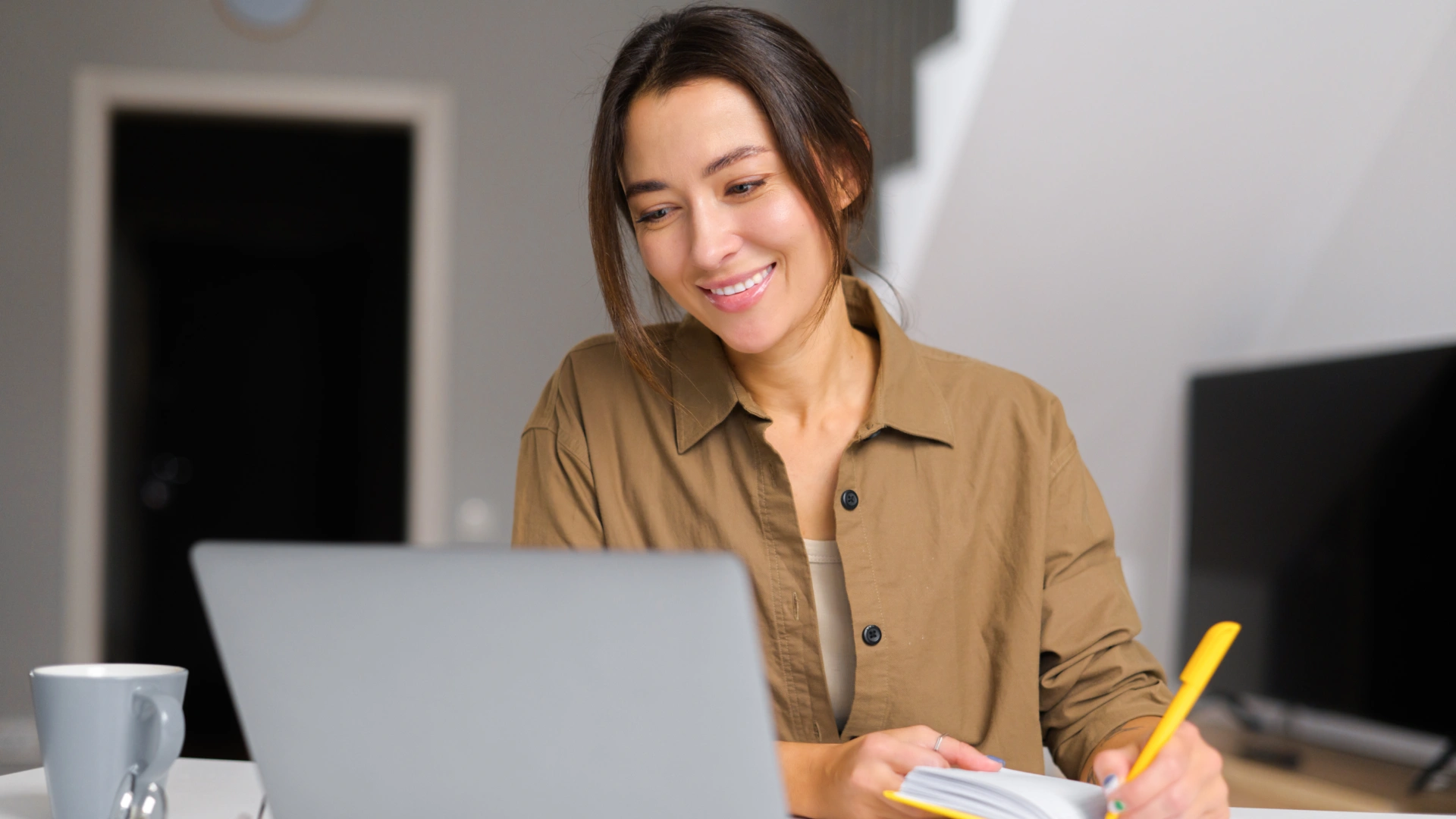Mulher sorridente estudando ou trabalhando em casa com notebook e caderno