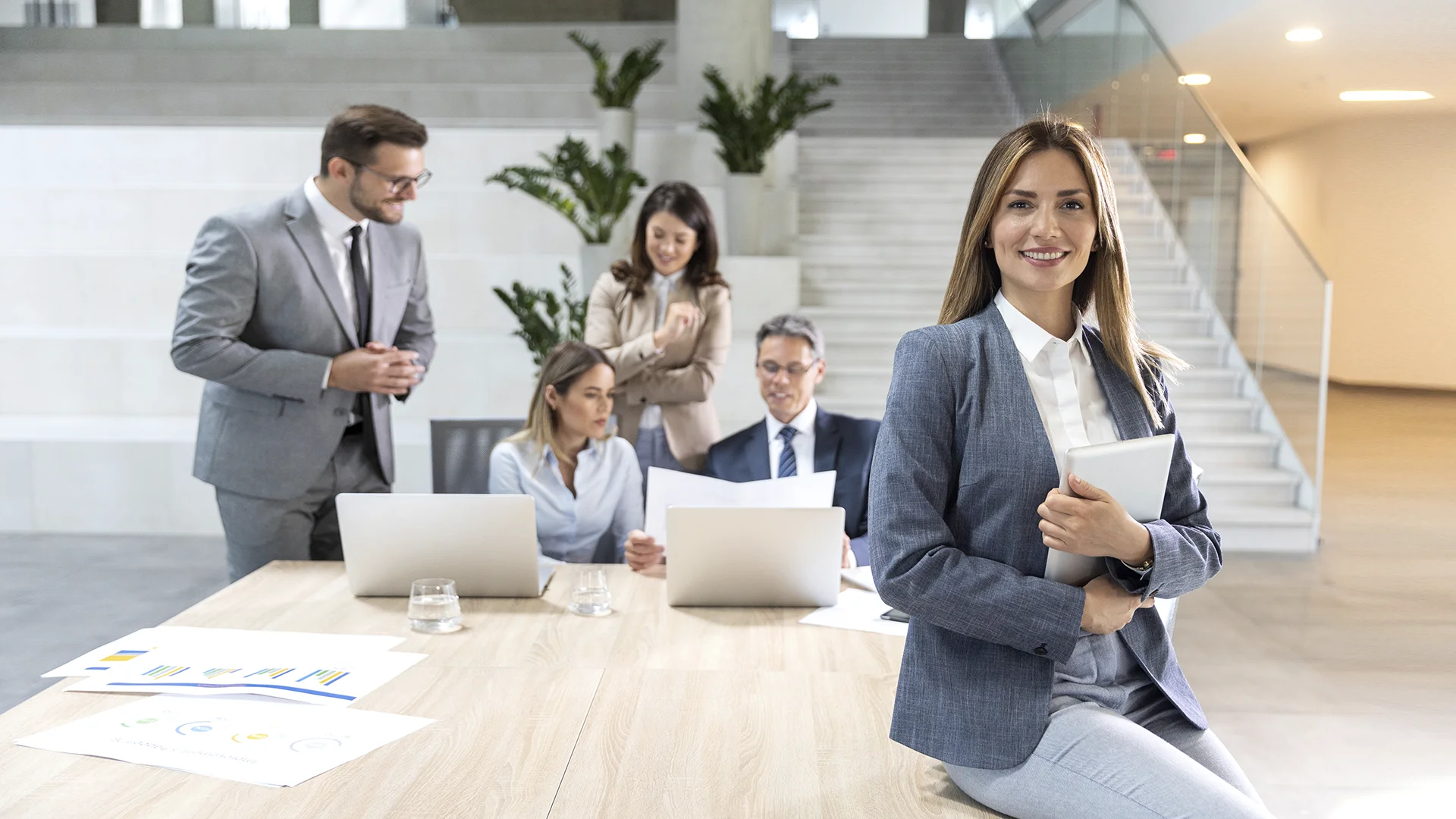 Mulher de negócios sorrindo em primeiro plano com equipe trabalhando ao fundo em um escritório moderno