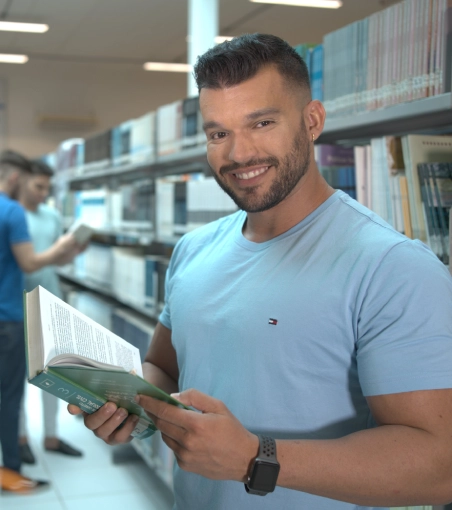 Jovem estudante sorridente lendo um livro em uma biblioteca universitária