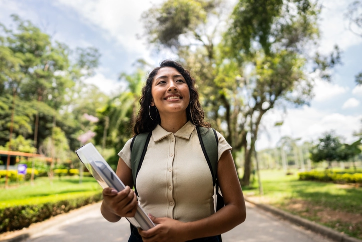 Estudante universitária sorridente caminhando no campus com mochila e livros