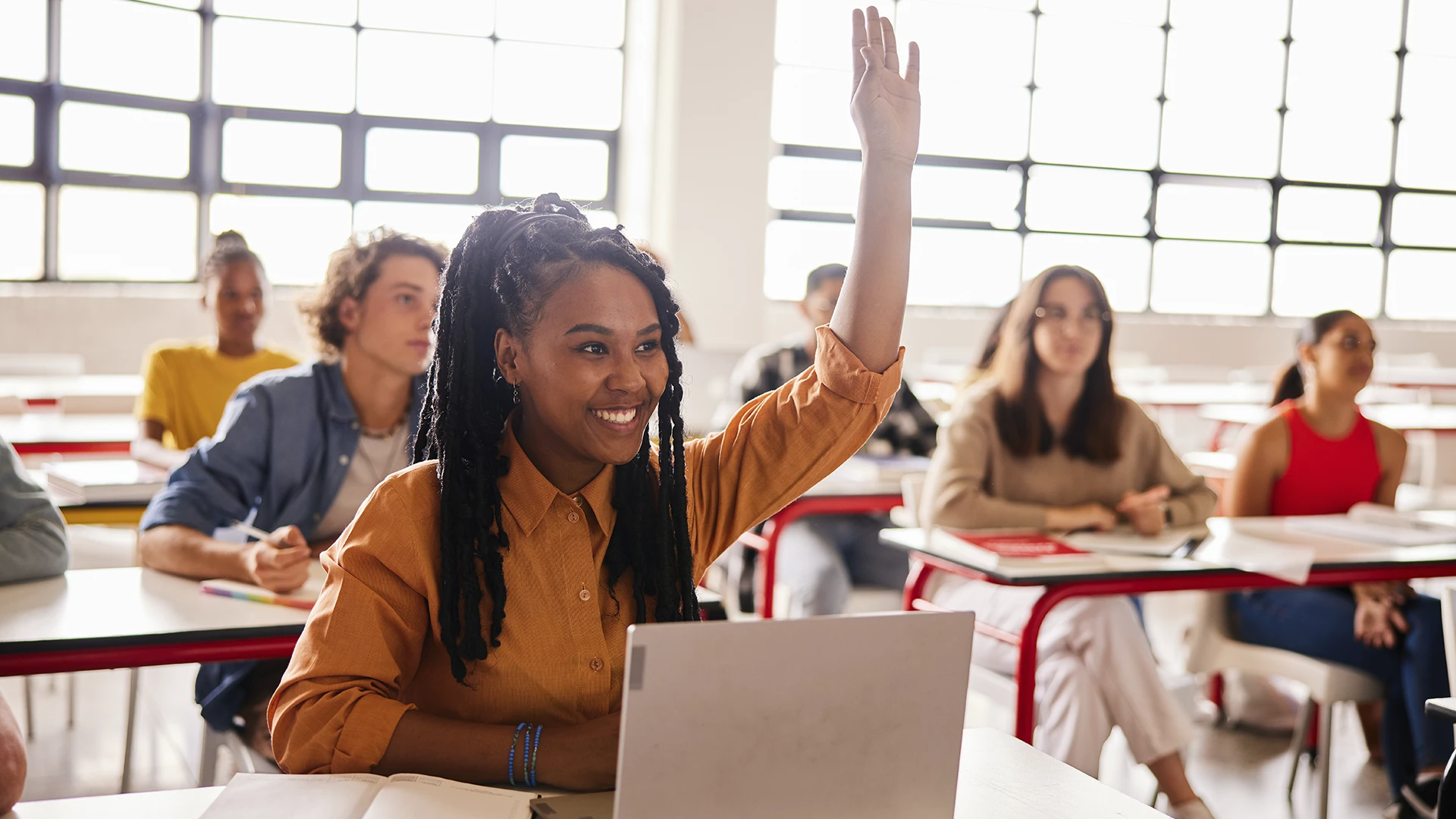Estudante universitária sorrindo com a mão levantada na sala de aula