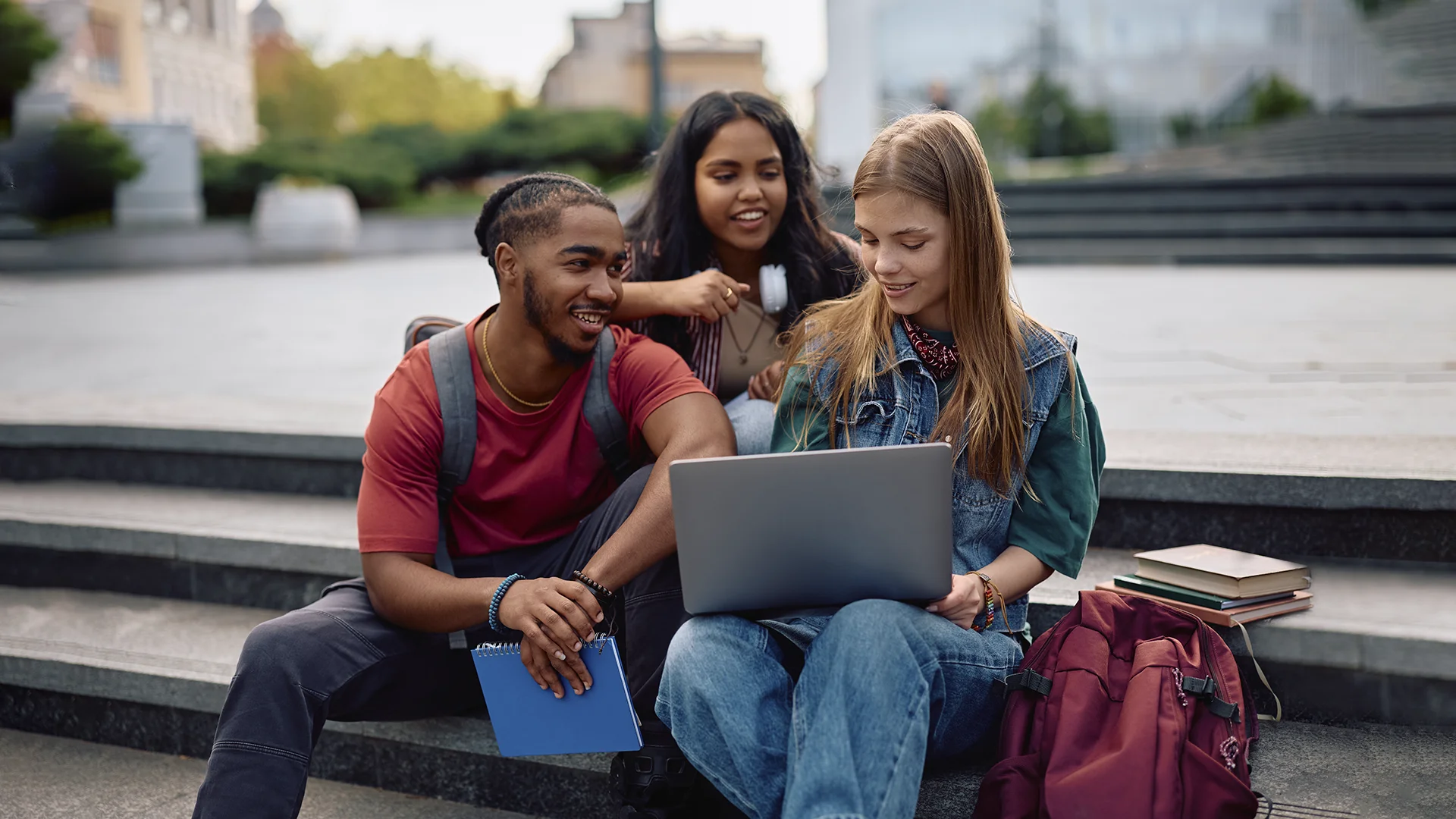 Grupo de estudantes universitários diversos estudando com laptop em escadaria ao ar livre