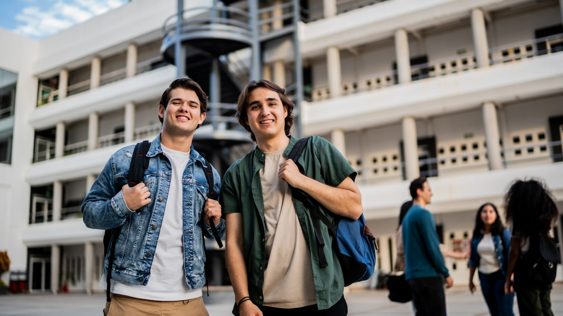 Dois jovens estudantes universitários sorrindo em um campus moderno, representando a vida acadêmica e a diversidade estudantil