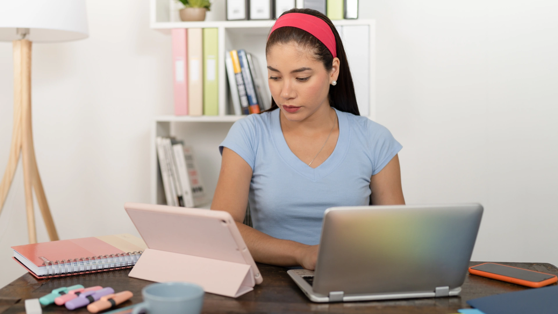 Estudante jovem focada usando notebook e tablet em uma mesa de estudos organizada