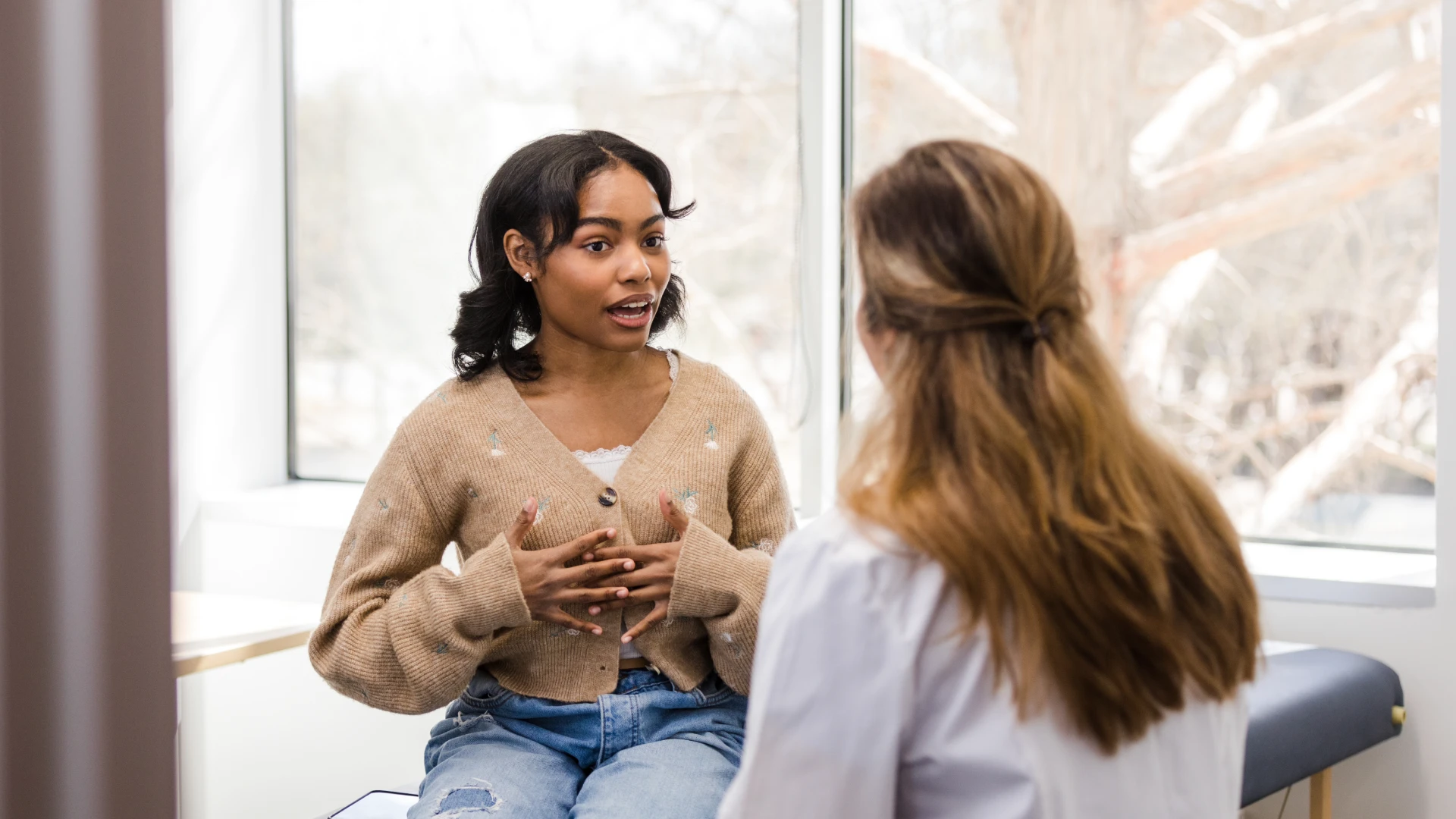 Paciente jovem em consulta médica conversando com profissional de saúde sobre seus sintomas em um ambiente clínico acolhedor