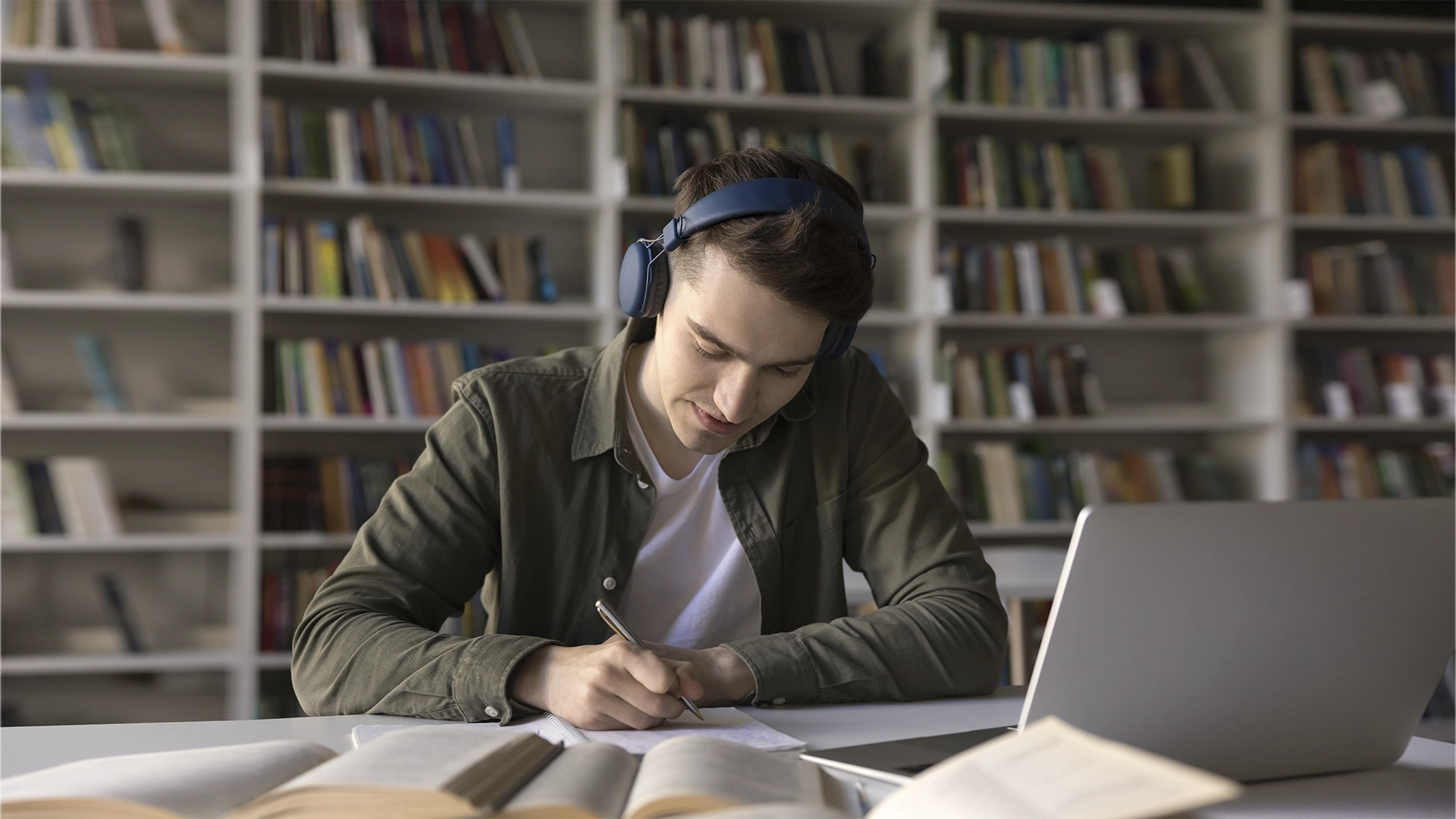 Estudante universitário com fones de ouvido escrevendo em um caderno em uma biblioteca