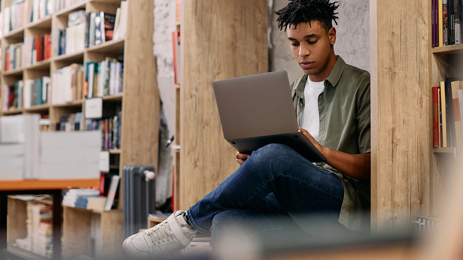 Estudante jovem usando laptop em uma biblioteca com estantes de livros ao fundo