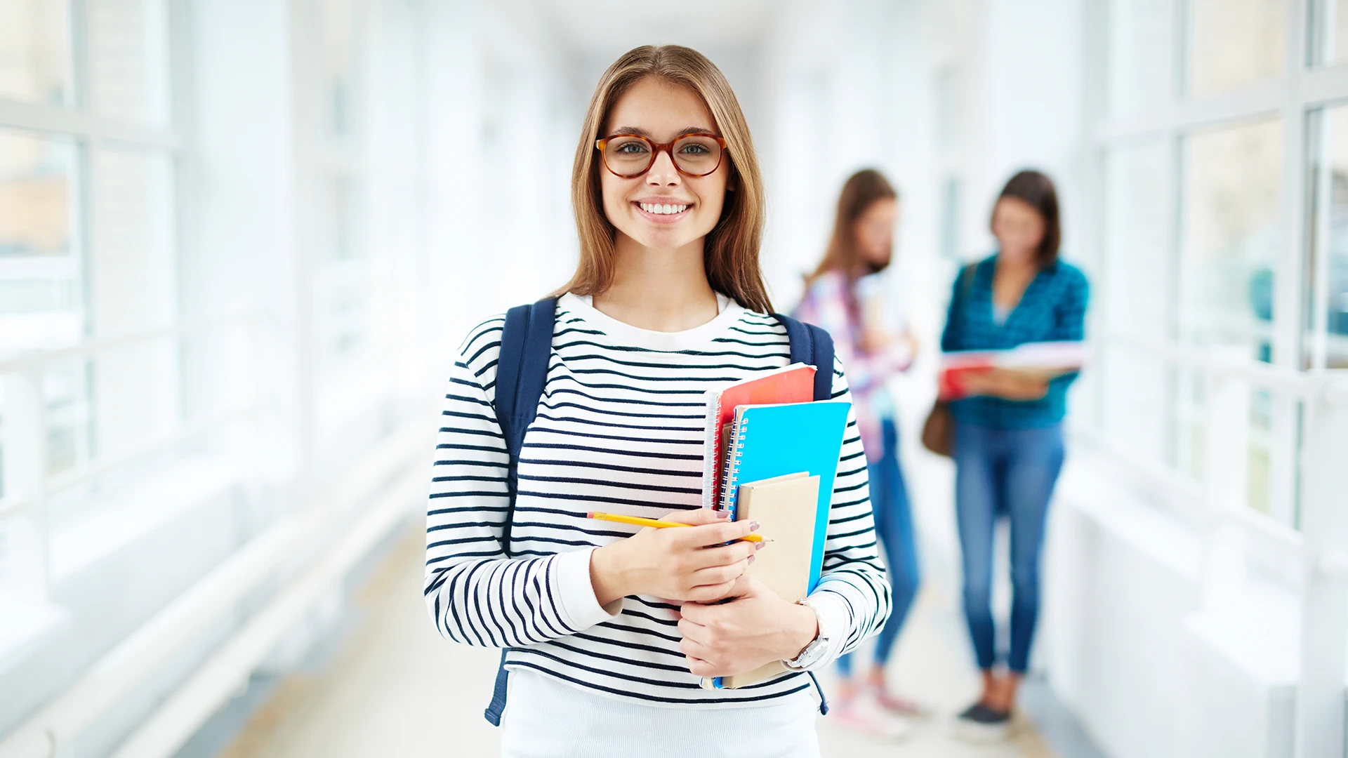 Estudante universitária sorridente segurando cadernos em um corredor de faculdade