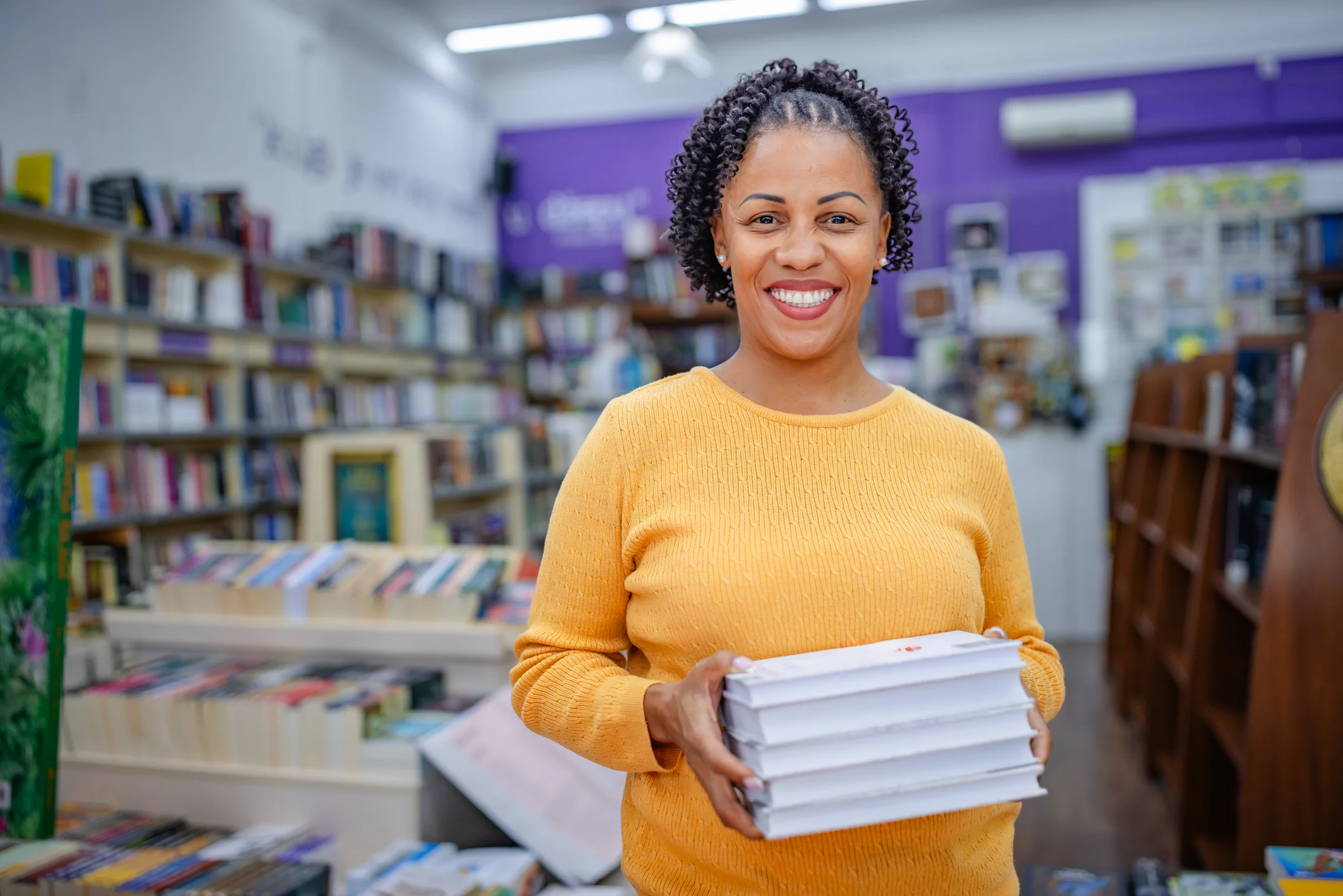 Mulher sorridente segurando uma pilha de livros em uma livraria