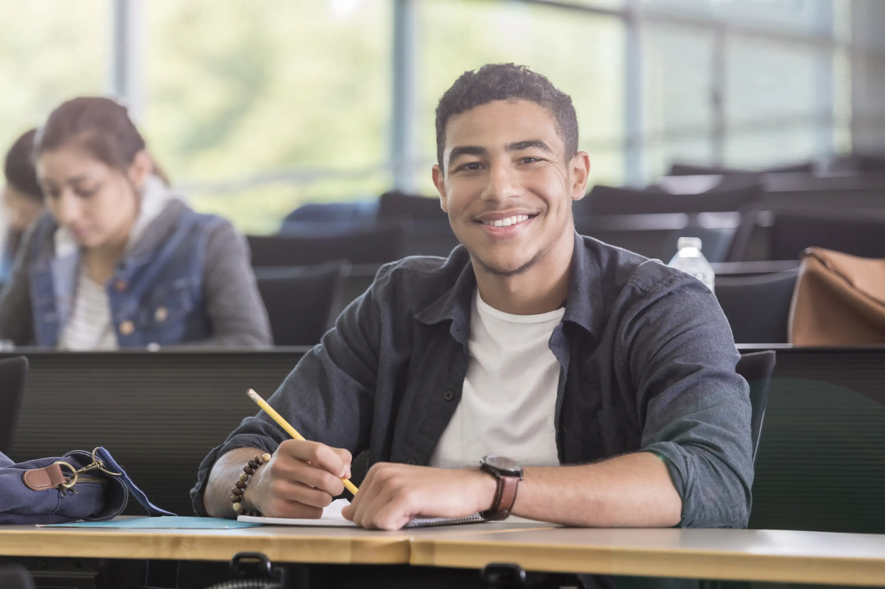 Estudante universitário sorridente sentado em uma sala de aula escrevendo em um caderno