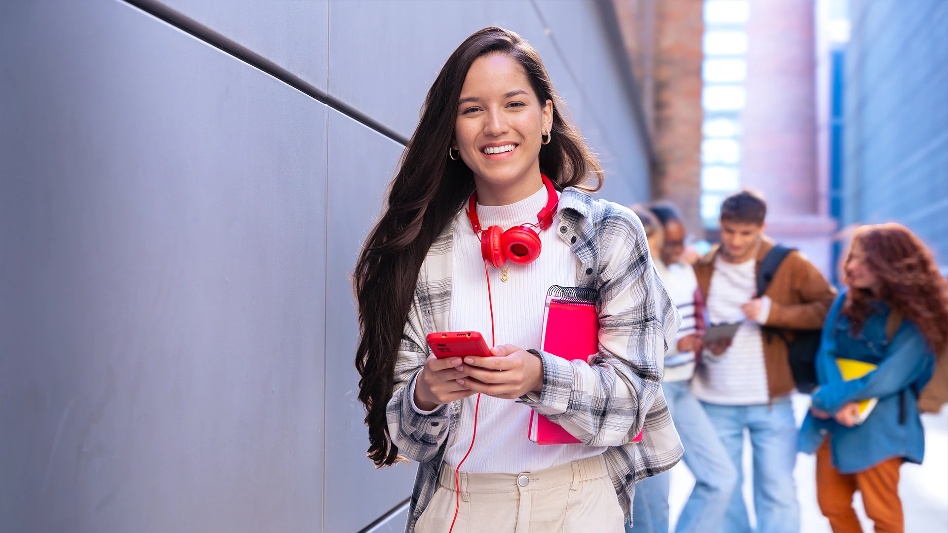 Estudante universitária sorridente segurando celular e caderno no campus