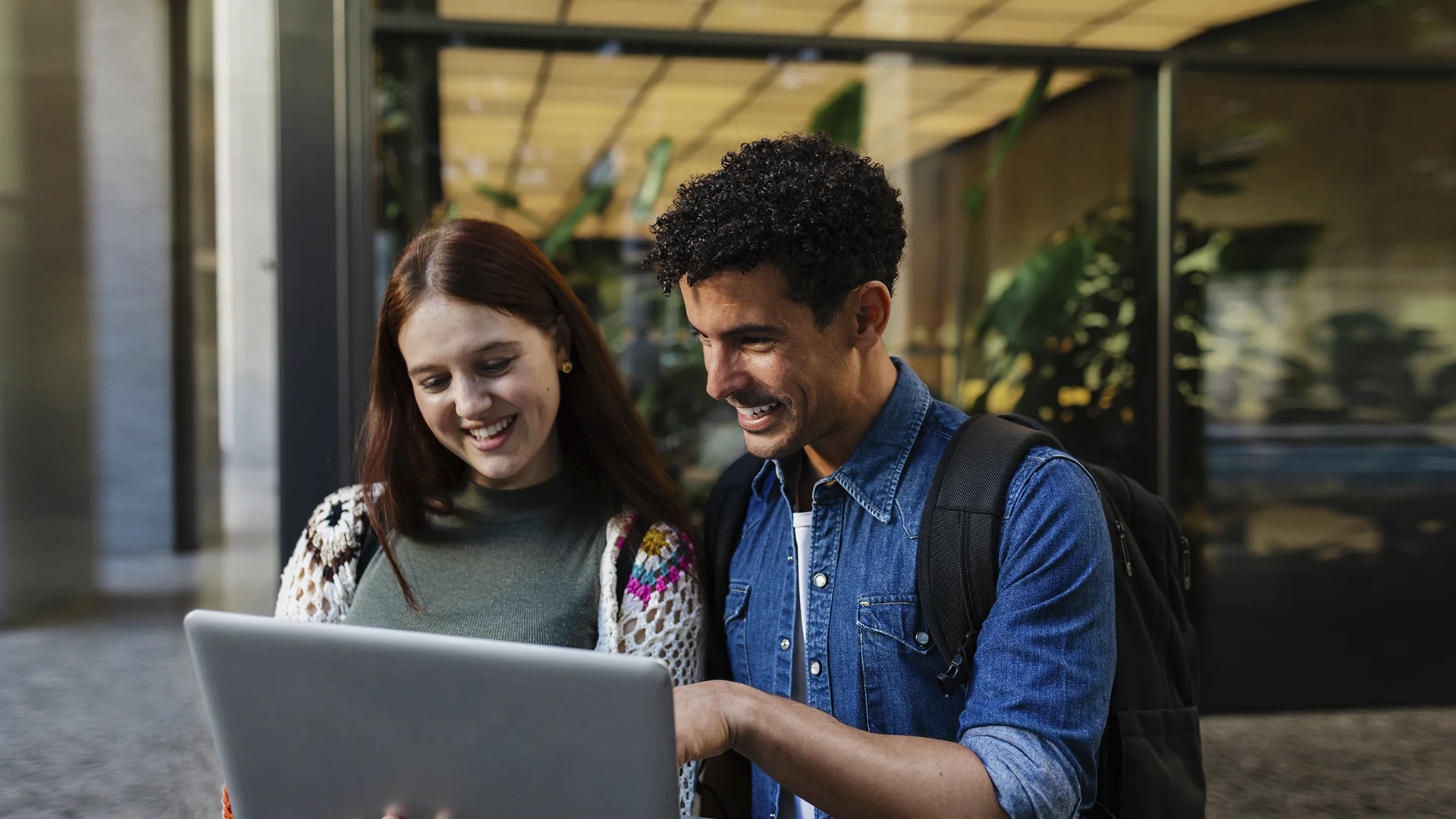 Estudantes universitários sorridentes usando um laptop juntos em um campus moderno
