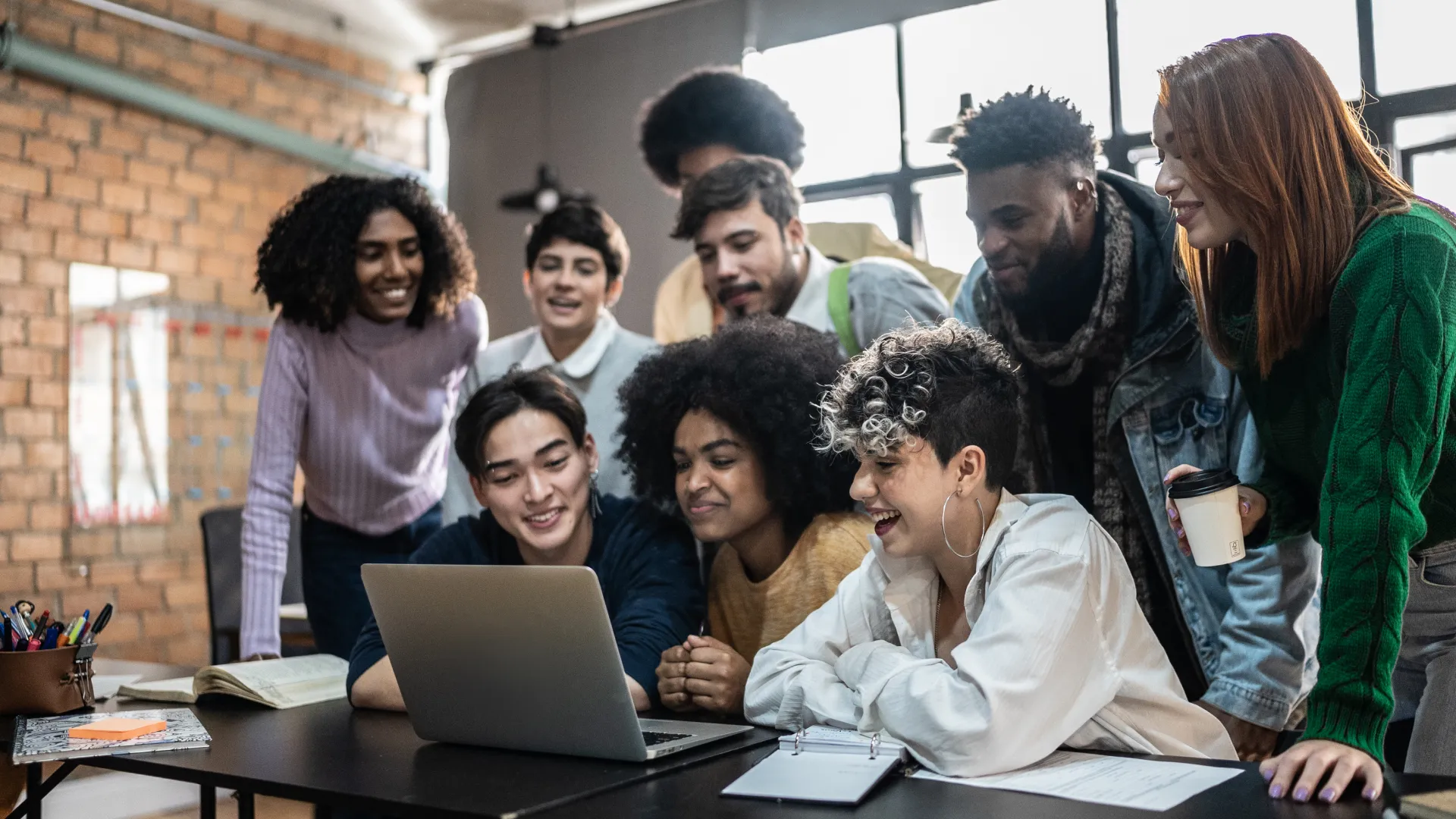 Grupo diversificado de estudantes universitários reunidos em torno de um notebook em um ambiente de colaboração