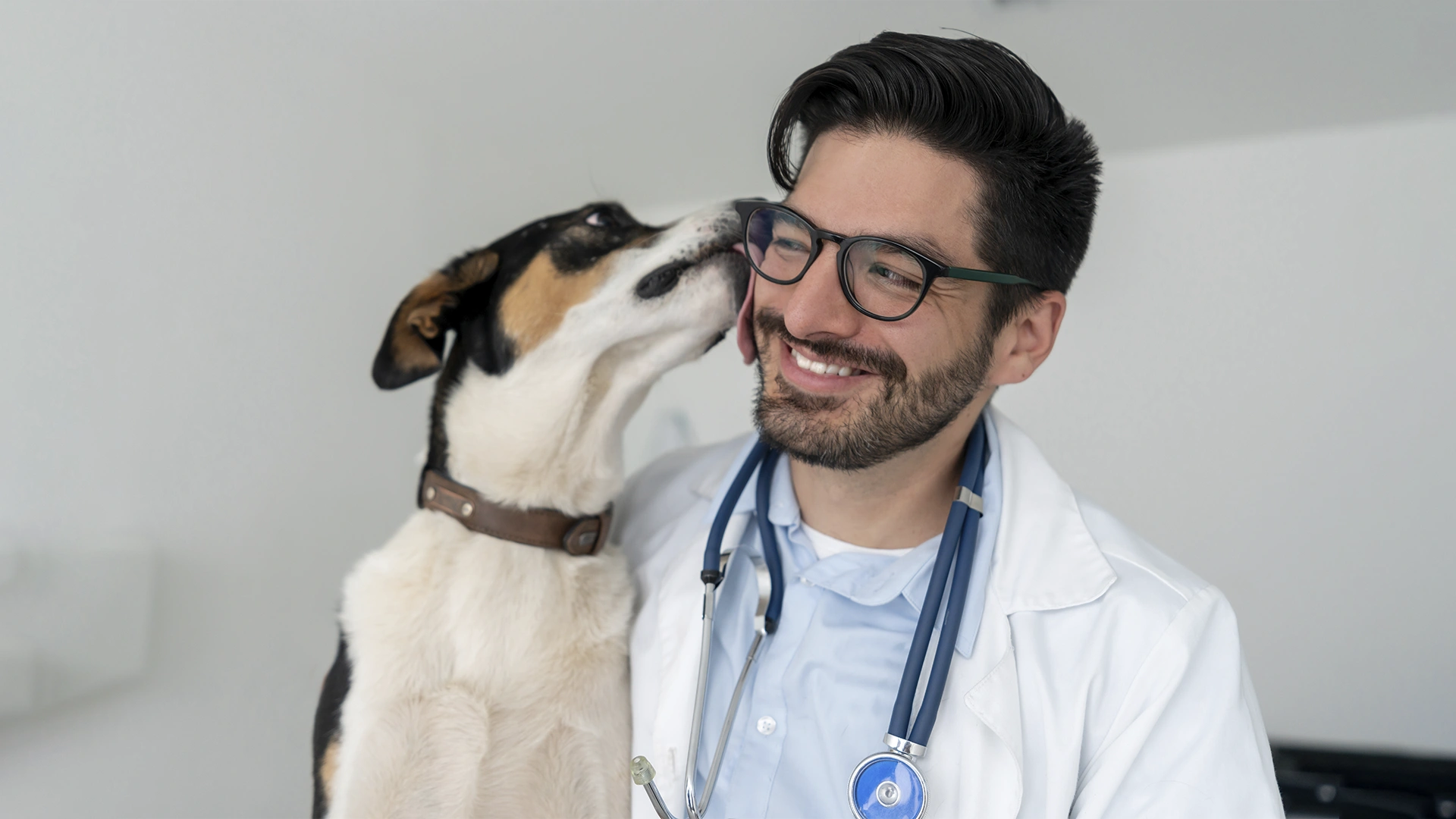 Veterinário sorrindo enquanto um cachorro lambe seu rosto em uma clínica veterinária