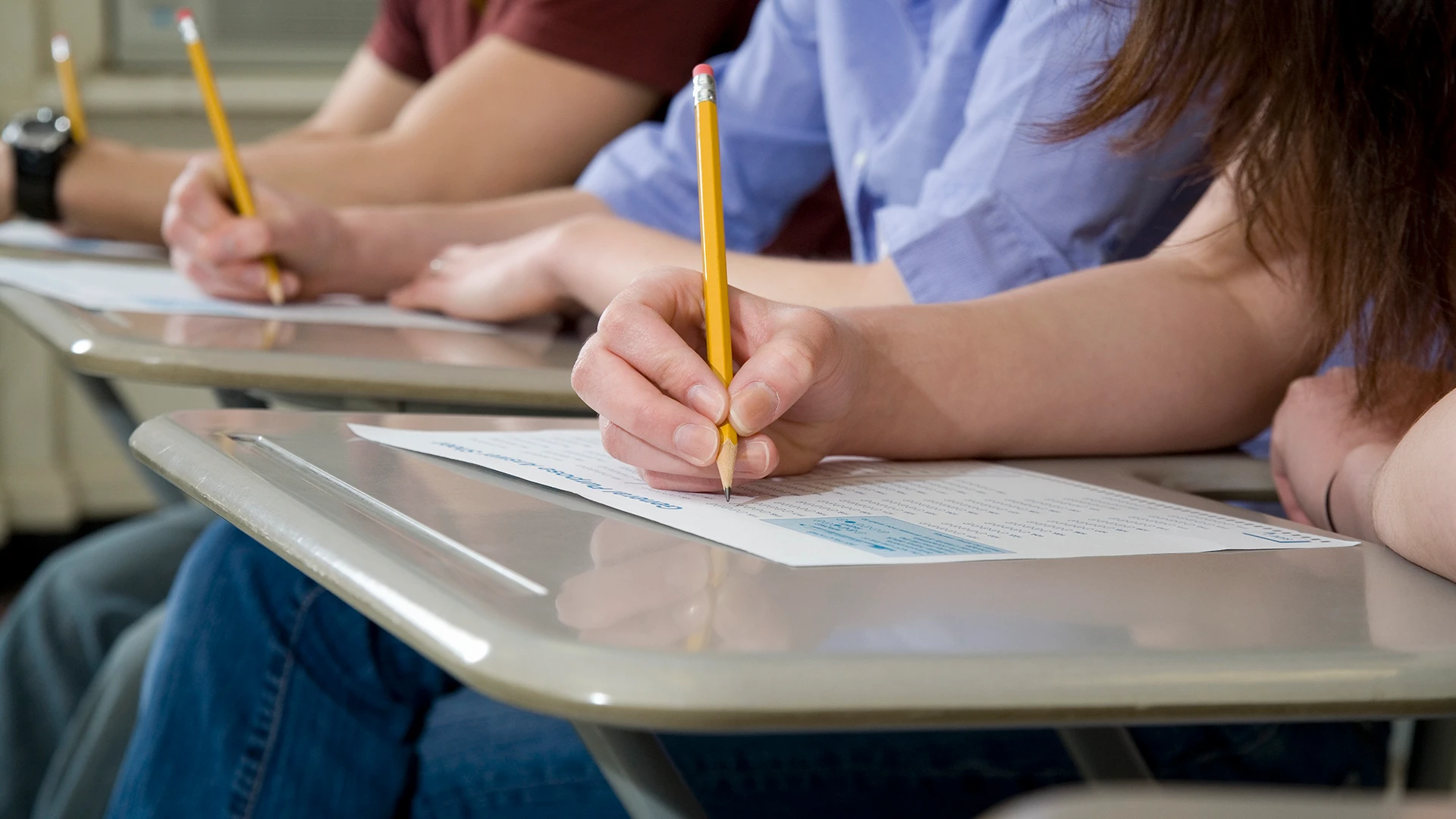 Estudantes concentrados realizando prova em sala de aula com lápis e papel.