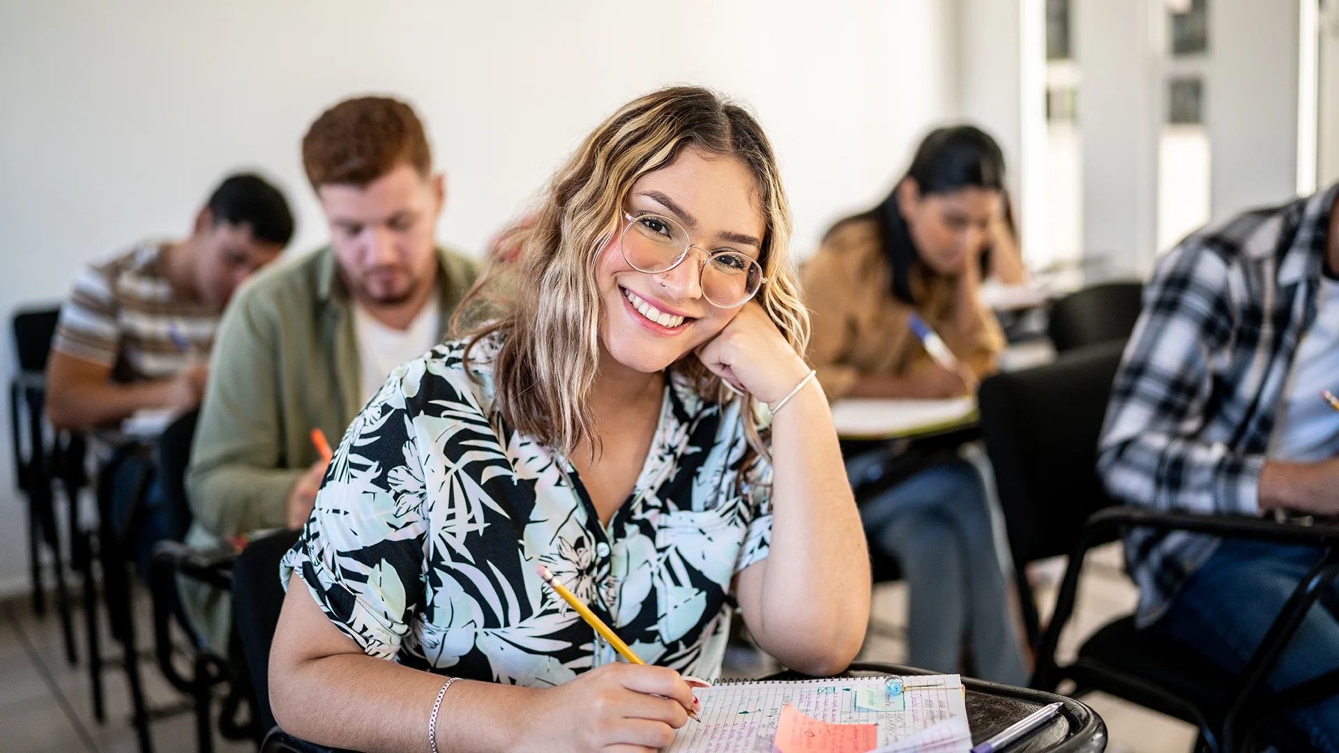 Estudante universitária sorrindo em sala de aula com colegas ao fundo