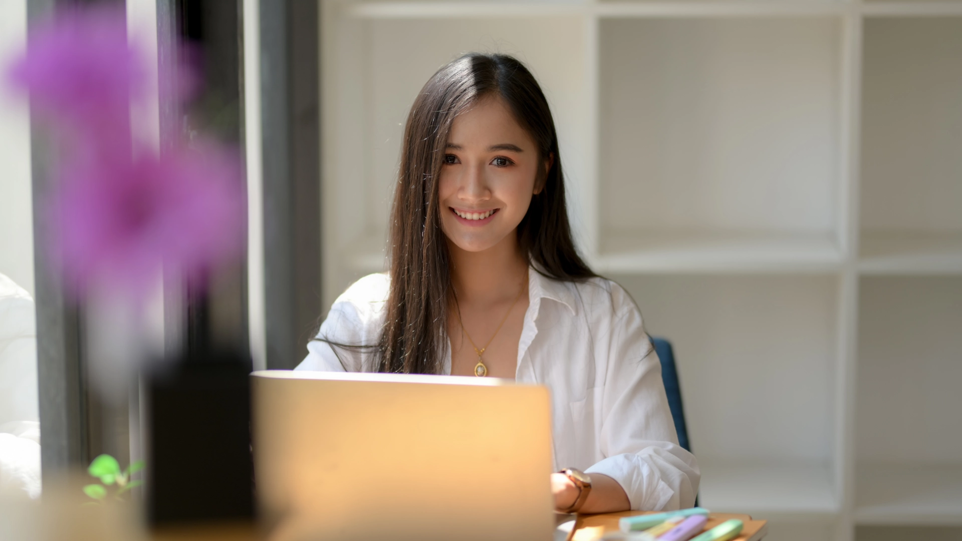 Jovem estudante sorridente usando laptop para estudar em um ambiente iluminado