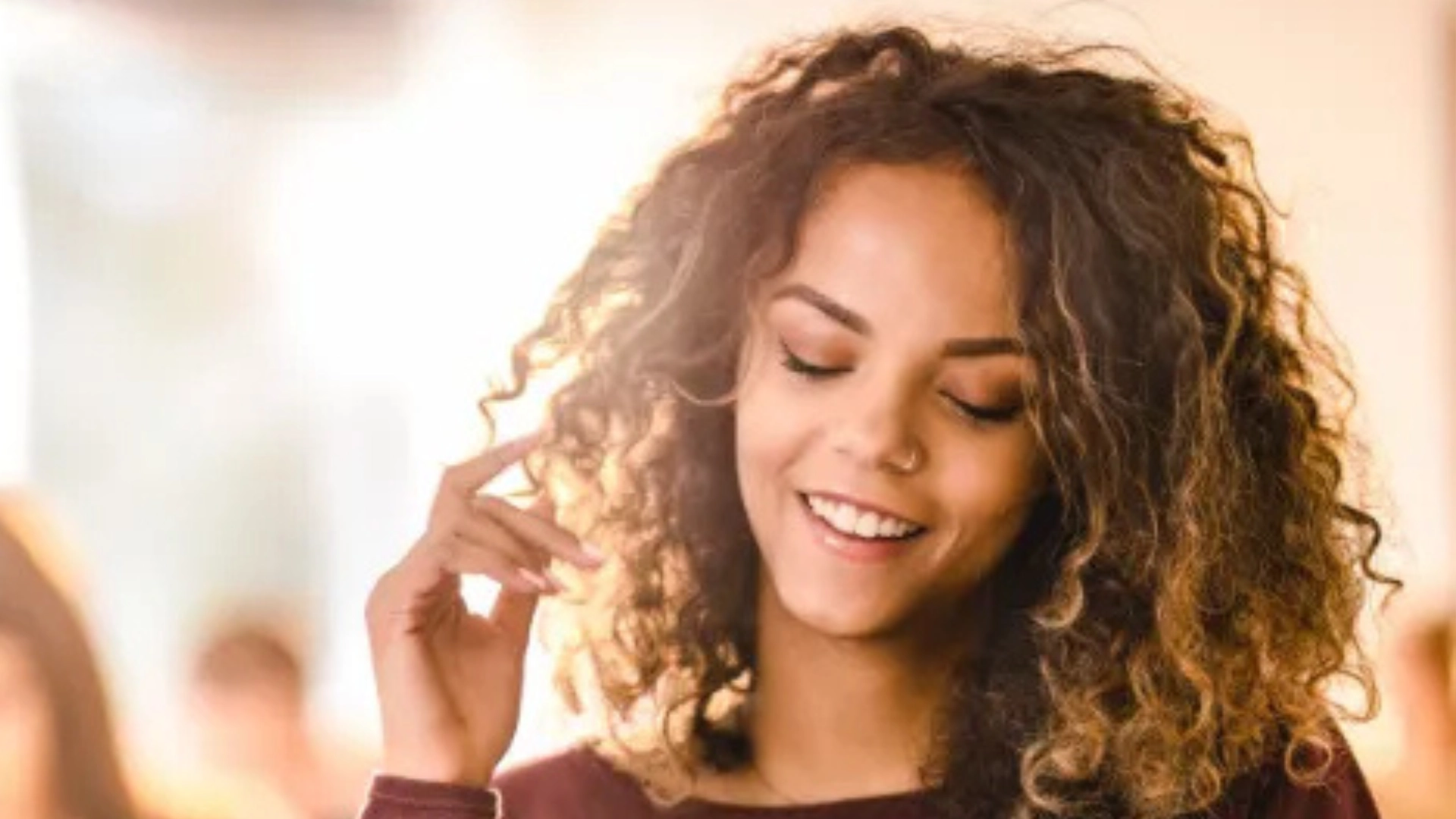 Jovem mulher sorridente com cabelos cacheados iluminada pela luz do sol