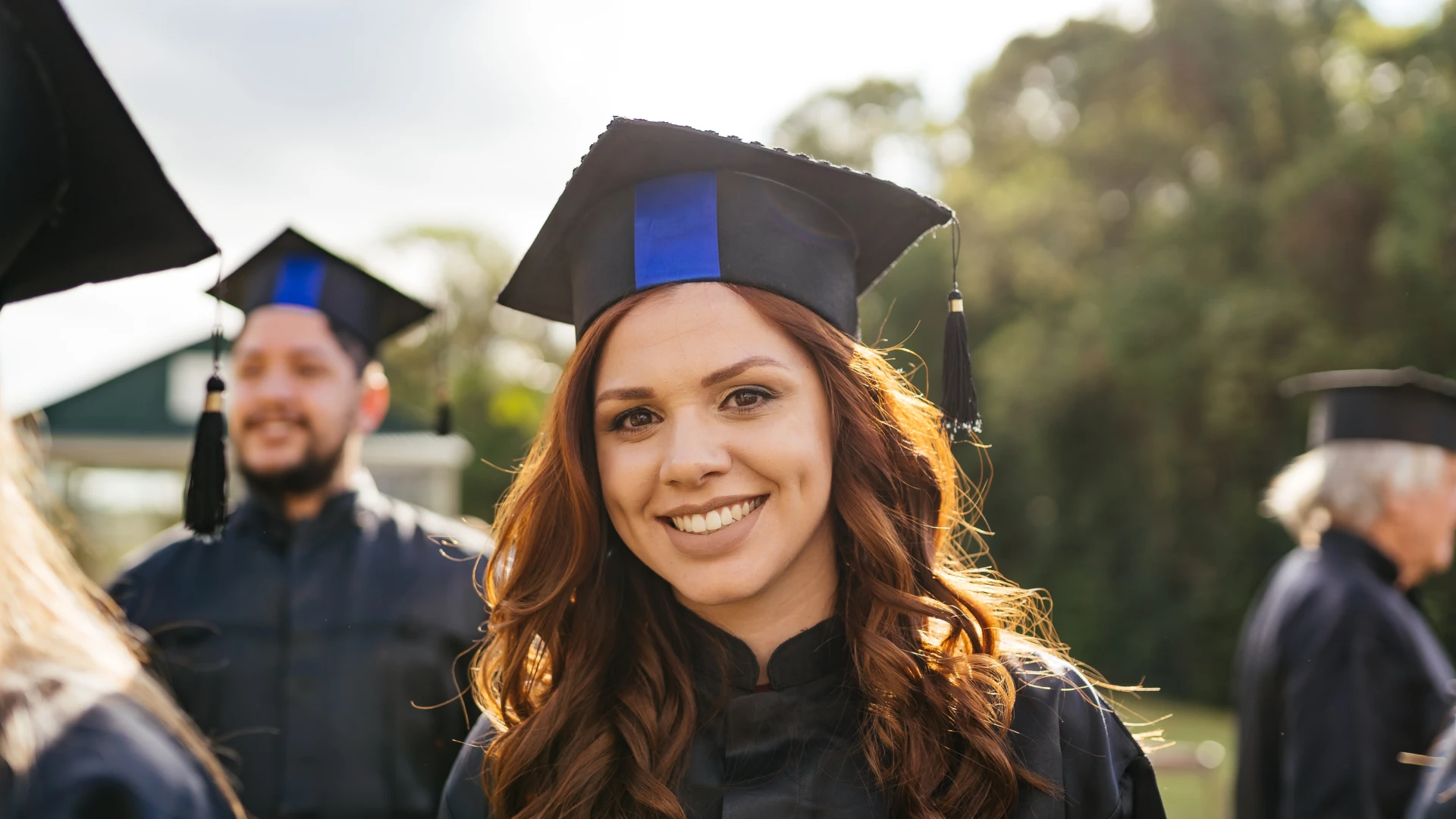 Estudante sorridente usando beca e capelo em cerimônia de formatura ao ar livre