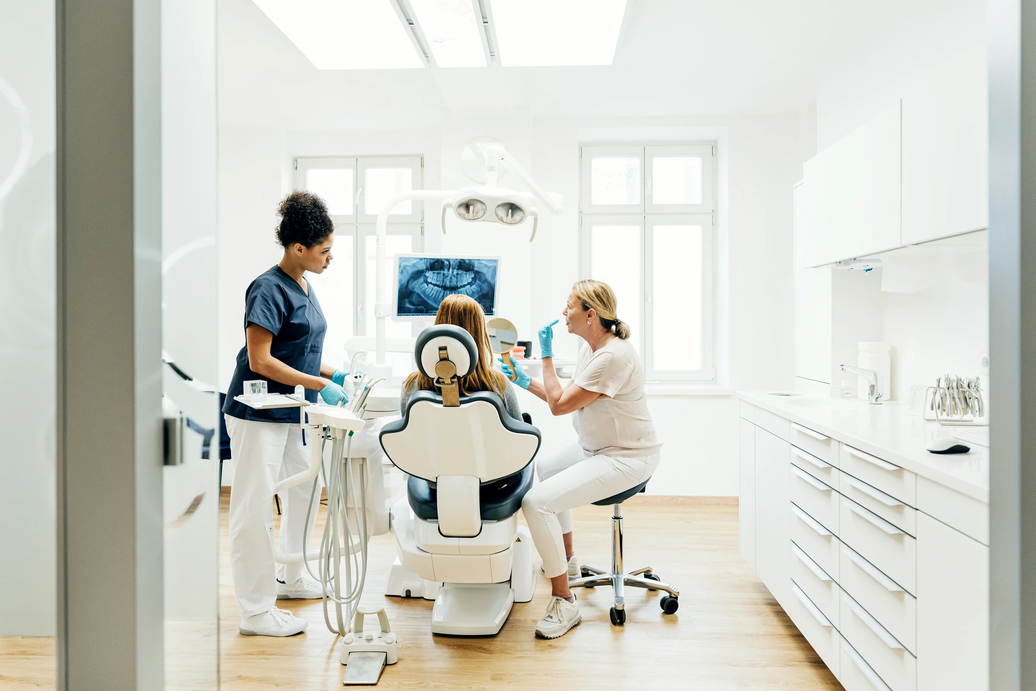 Dentista e auxiliar atendendo paciente em consultório odontológico moderno com radiografia panorâmica