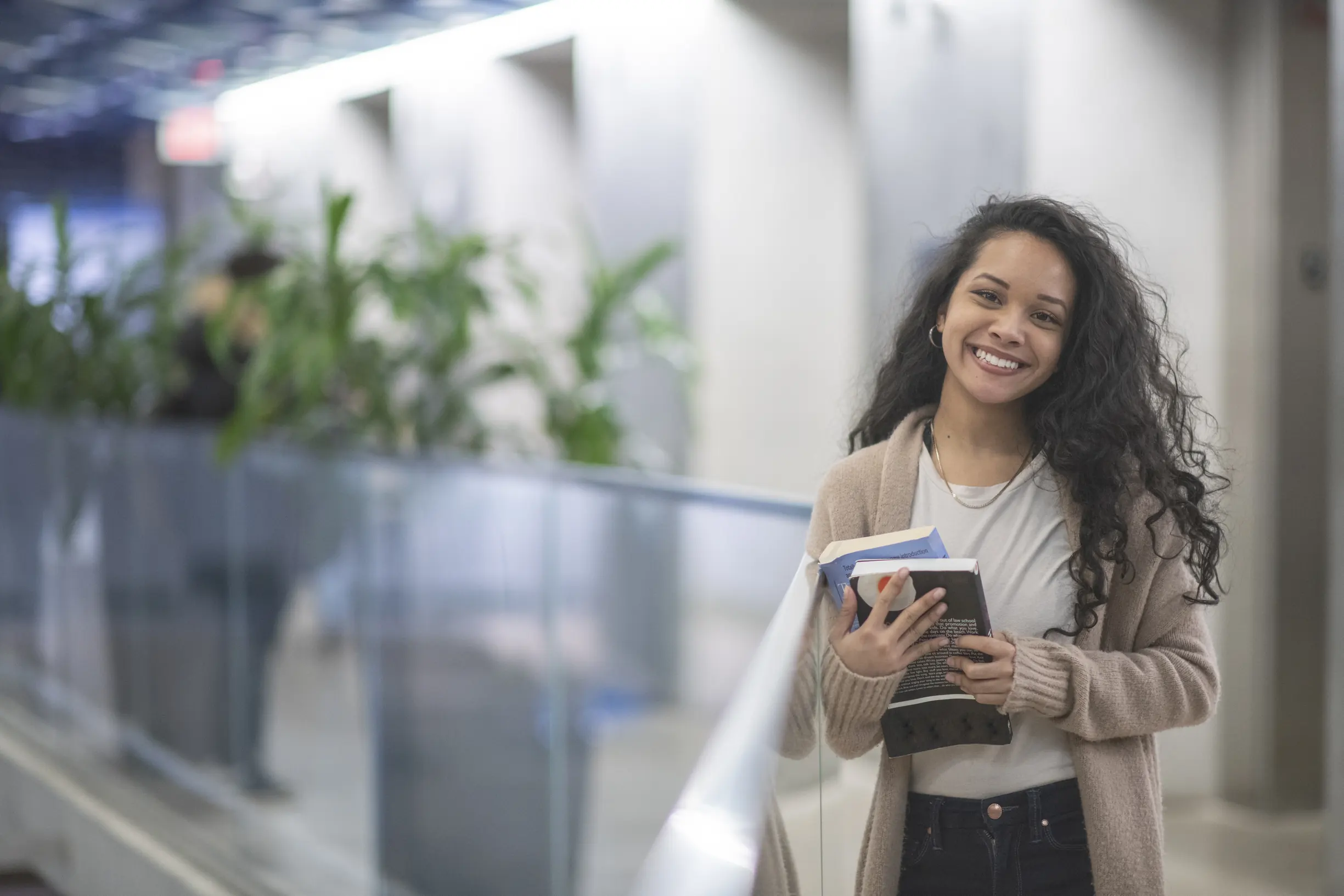 Estudante universitária sorridente segurando livros em um corredor moderno de campus