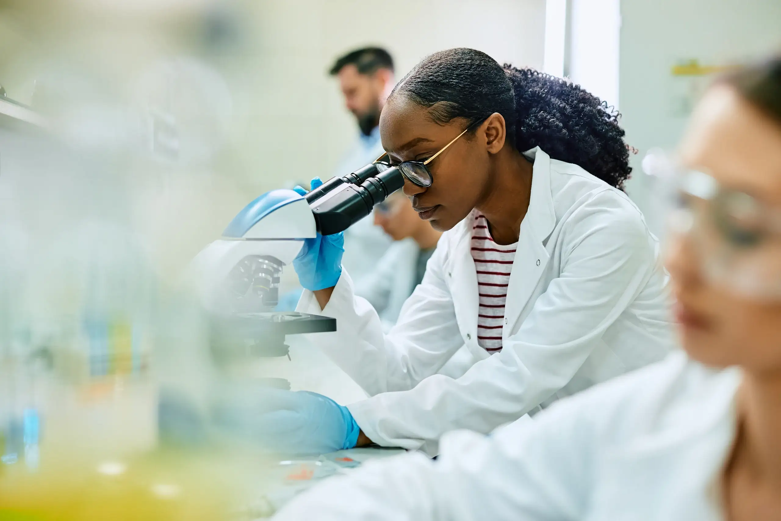 Pesquisadora focada realizando análises científicas com microscópio em um ambiente de laboratório universitário moderno