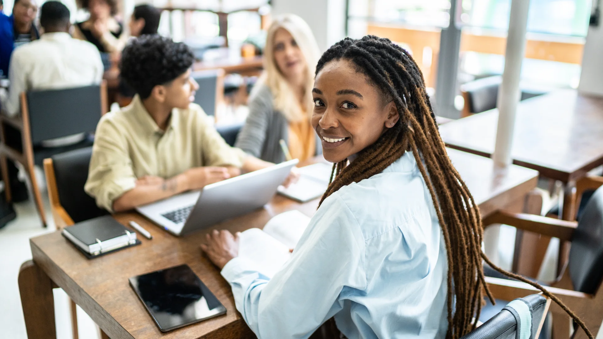 Estudante universitária sorrindo durante trabalho em grupo com colegas em ambiente de estudos