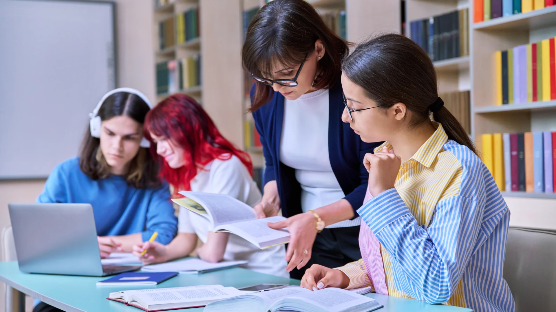 Professora auxiliando alunos em seus estudos acadêmicos e pesquisas na biblioteca de uma faculdade