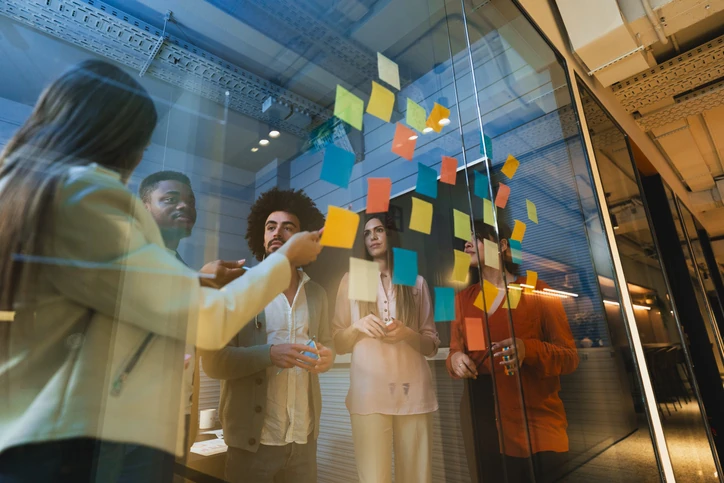 Equipe diversa colaborando em um brainstorming com post-its coloridos em uma parede de vidro em um escritório moderno