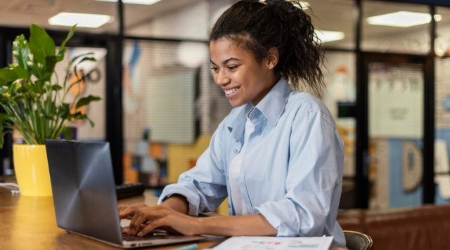 Estudante jovem e sorridente utilizando um notebook em um ambiente de escritório moderno