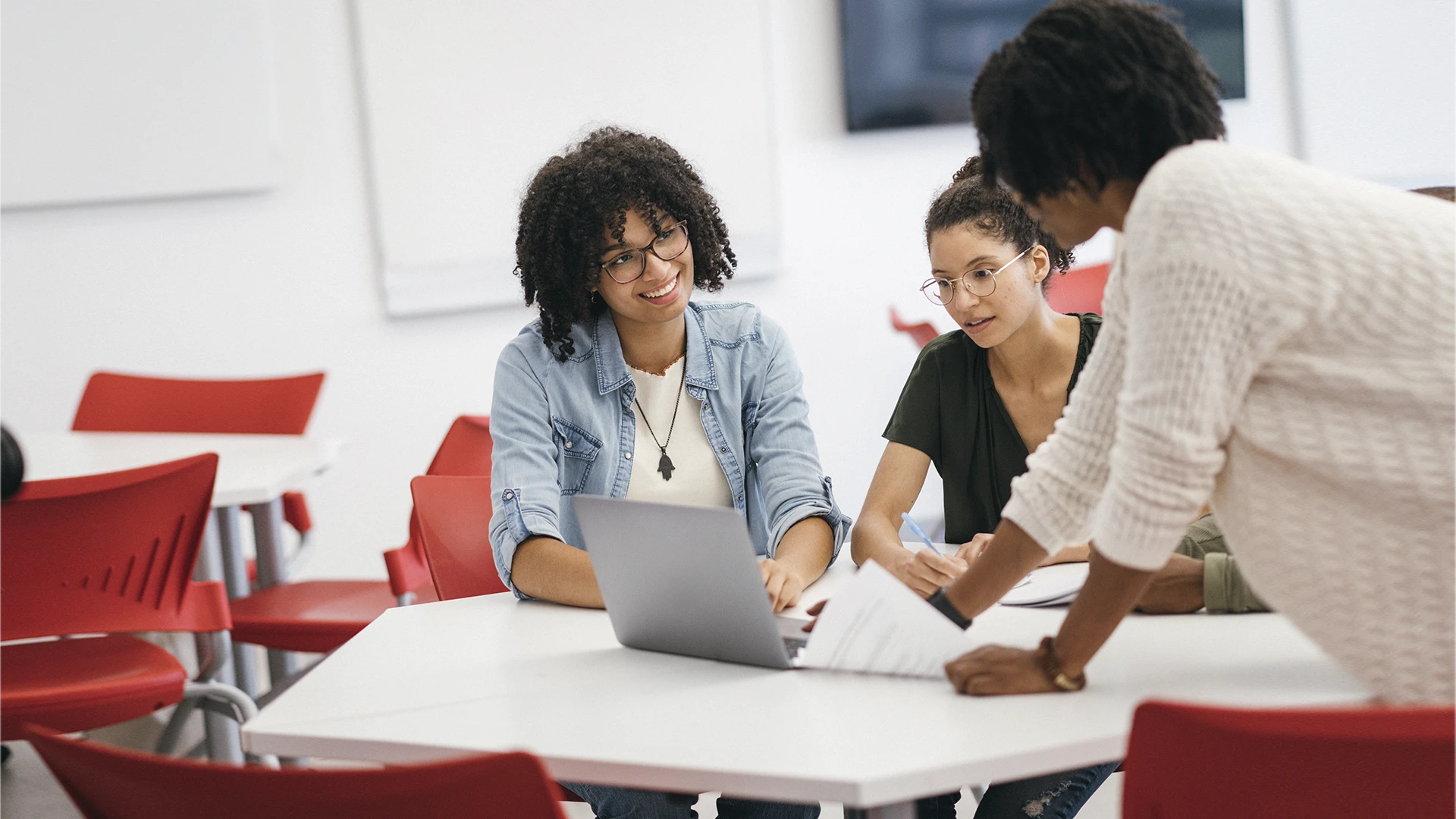 Grupo de estudantes universitárias colaborando em um projeto acadêmico usando um laptop em sala de aula